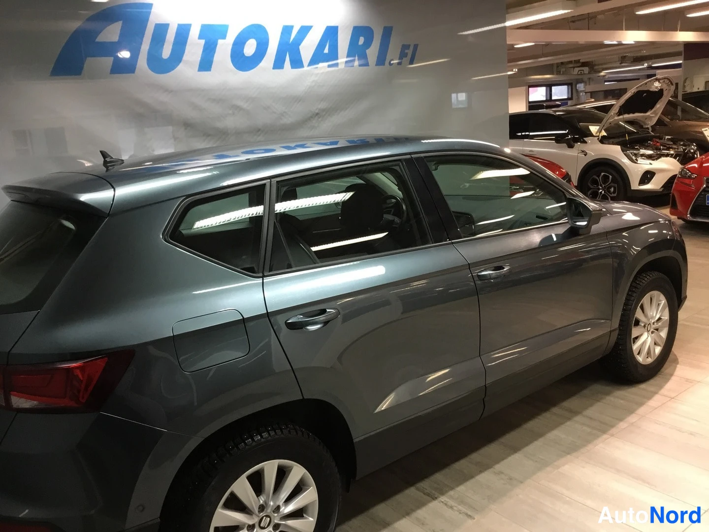 Takaviisto: Tummanharmaan SEAT Atecan takakolmannesvasen kylki autonäyttelytilassa, taustalla muita ajoneuvoja.