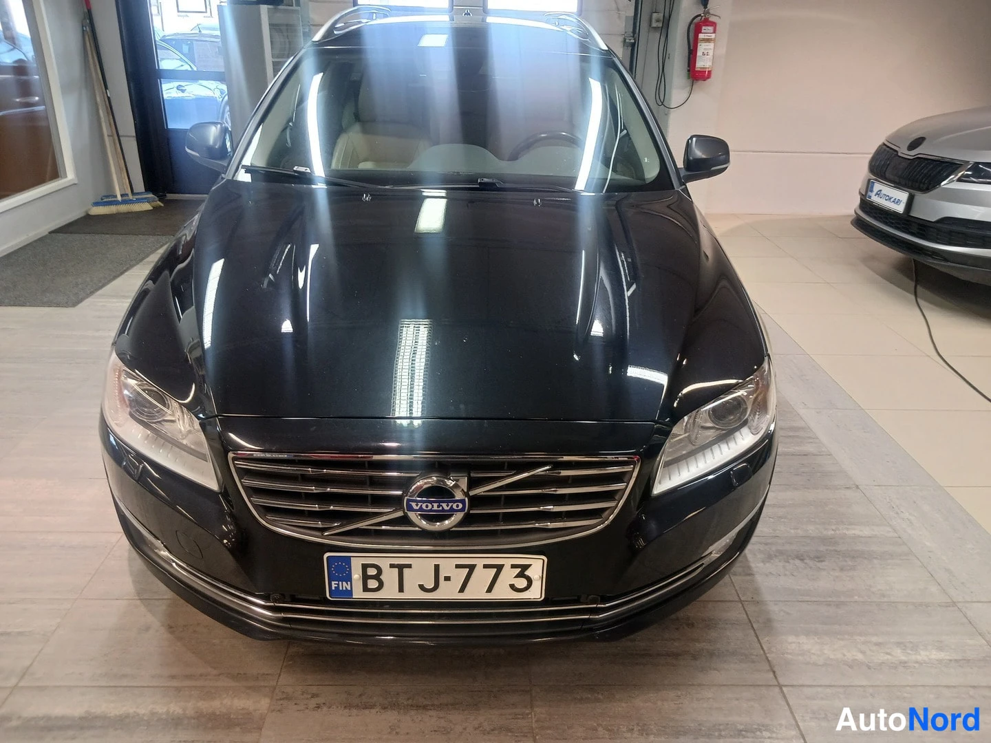 Edestä: Mustan farmariauton etupää suoraan edestä kuvattuna; Volvo-merkki säleikössä ja rekisterikilpi.