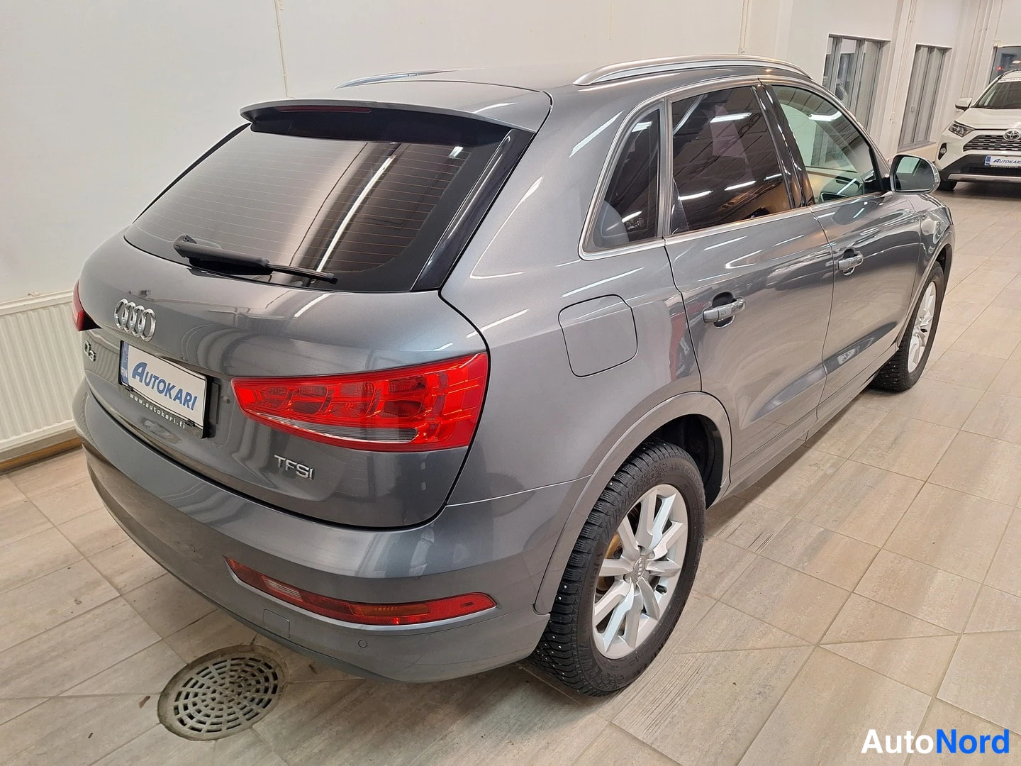 Takaviisto: Harmaan Audi Q3:n takaosa viistosti vasemmalta, TFSI-merkintä takaluukussa ja Autokari-kilpi.