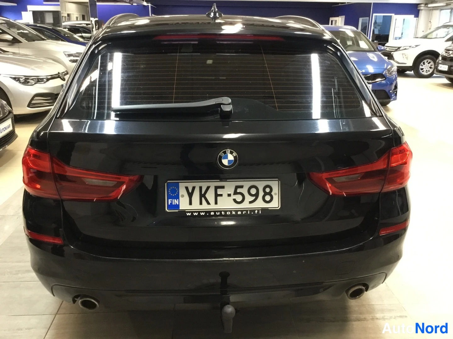 Takaa: Auton takaosa suoraan takaa kuvattuna; tumma BMW, punaiset takavalot, savuke­suuttimet takapuskurissa ja rekisteritunnus tekstillä www.autokari.fi.