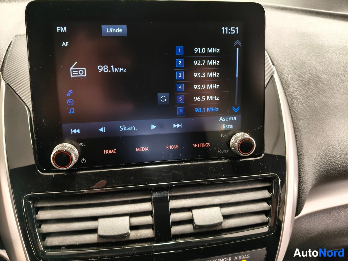 Etuviisto, nokka vasemmalle: Radio on FM-vastaanottotilassa näyttäen kanavaluettelon 91.0 MHz:stä 98.1 MHz:ään sekä toimintopainikkeet HOME, MEDIA, PHONE ja SETTINGS.