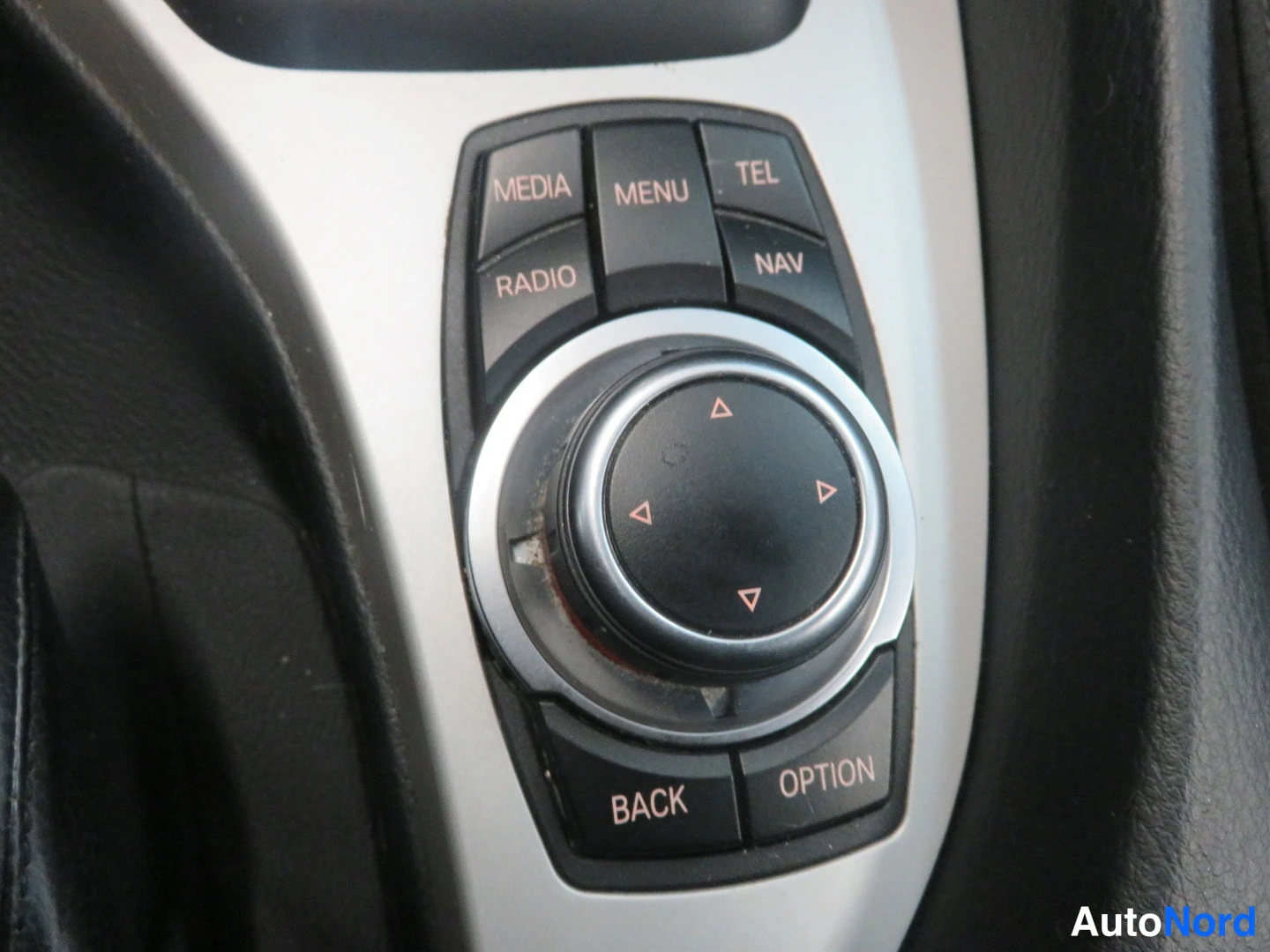 Yksityiskohta: BMW:n iDrive-ohjainkiekko, jonka ympärillä MEDIA-, MENU-, TEL-, RADIO-, NAV-, BACK- ja OPTION-painikkeet.