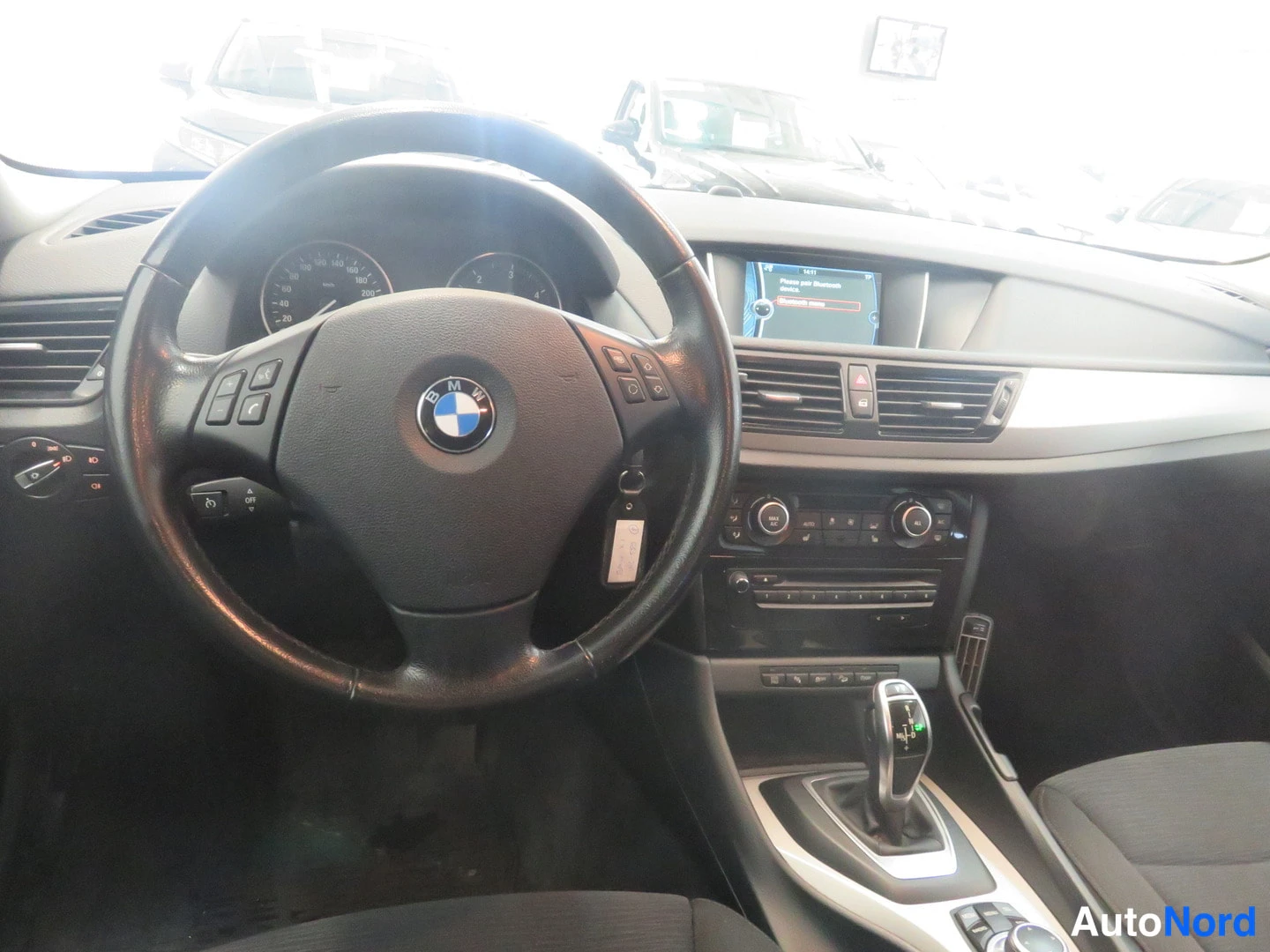 Muu: Ohjaamon näkymä: BMW-ohjauspyörä, mittaristo ja keskikonsoli näytöineen ja vaihtajan kanssa.