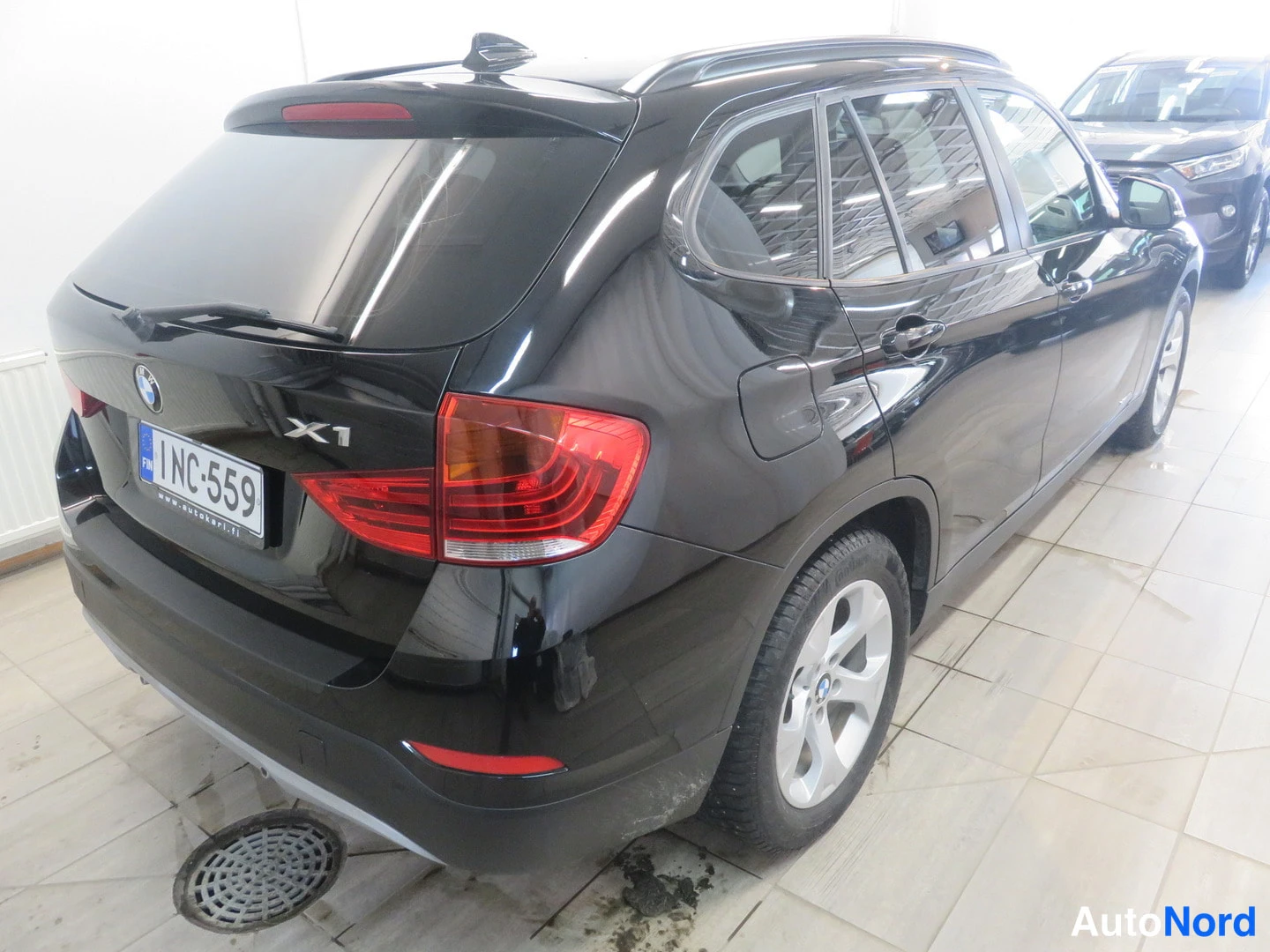 Takaviisto: BMW X1:n takapää ja oikea kylki kolmanneskulmassa, musta koriväri, takavalot ja -rekisterikilpi näkyvissä sisätiloissa.