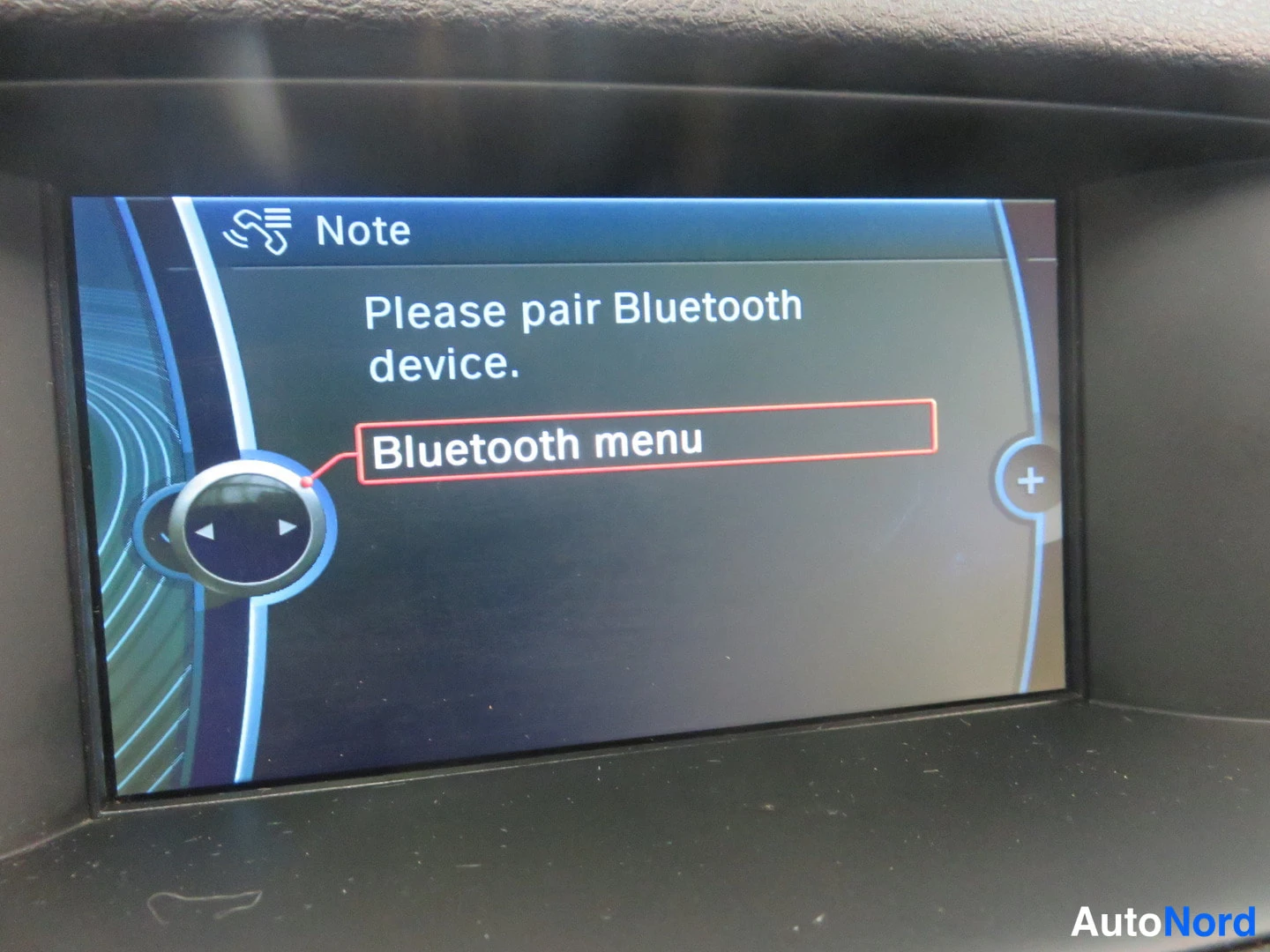 Yksityiskohta: Auton infotainment-näyttö näyttää viestin 'Please pair Bluetooth device' ja korostetun 'Bluetooth menu' -valinnan.