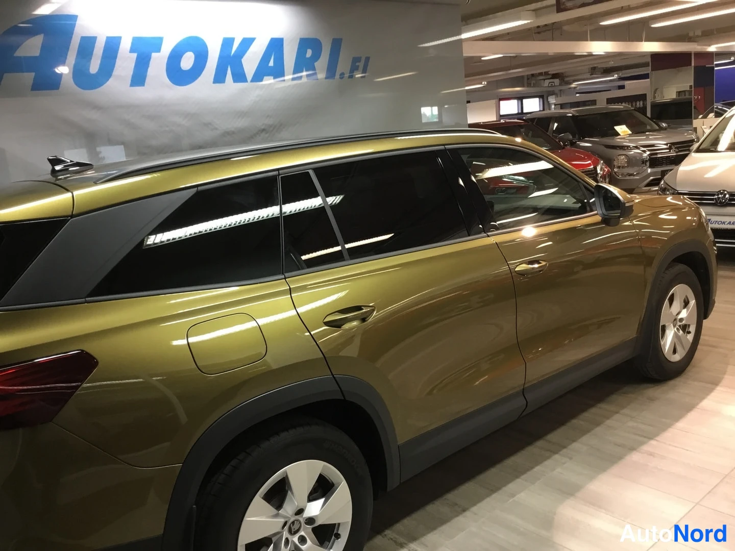 Sivulta: Kylkikuva vihreän-kultaisesta SUV:sta myymälässä, näkyvät ovienkahvat, takavalojen reuna ja hopeavanteet.