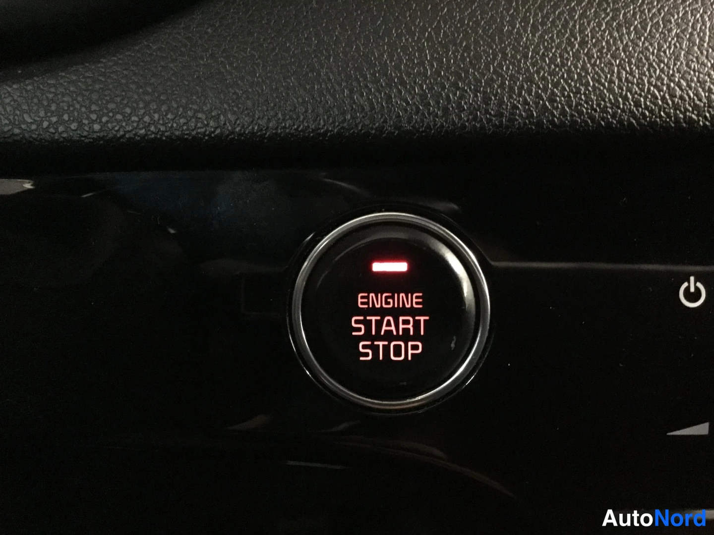 Yksityiskohta: Lähikuva auton käynnistyspainikkeesta, jossa lukee ENGINE START STOP ja punainen merkkivalo palaa.