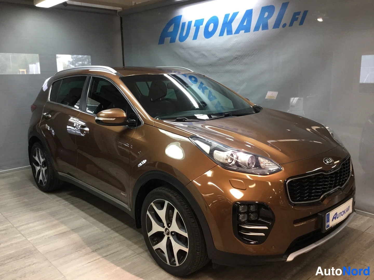 Etuviisto, nokka oikealle: Kia Sportage pronssinruskea etukulmasta oikealta sisätiloissa.