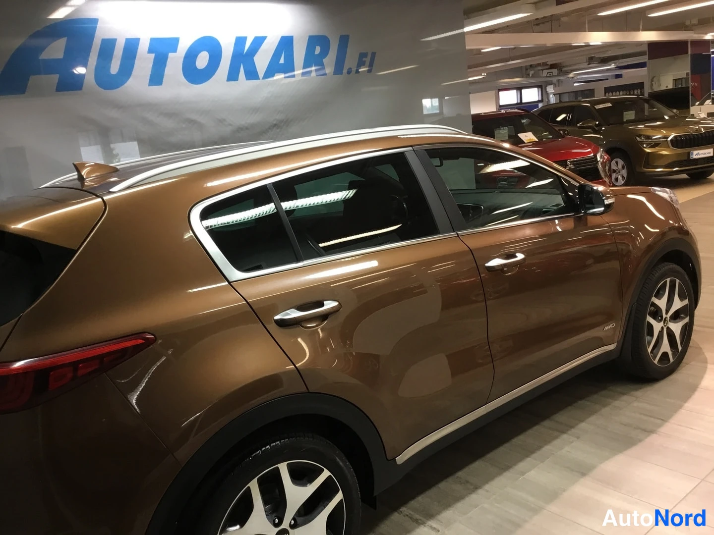 Takaviisto: Kia Sportage pronssinruskea takakulmasta vasemmalta sisätiloissa.