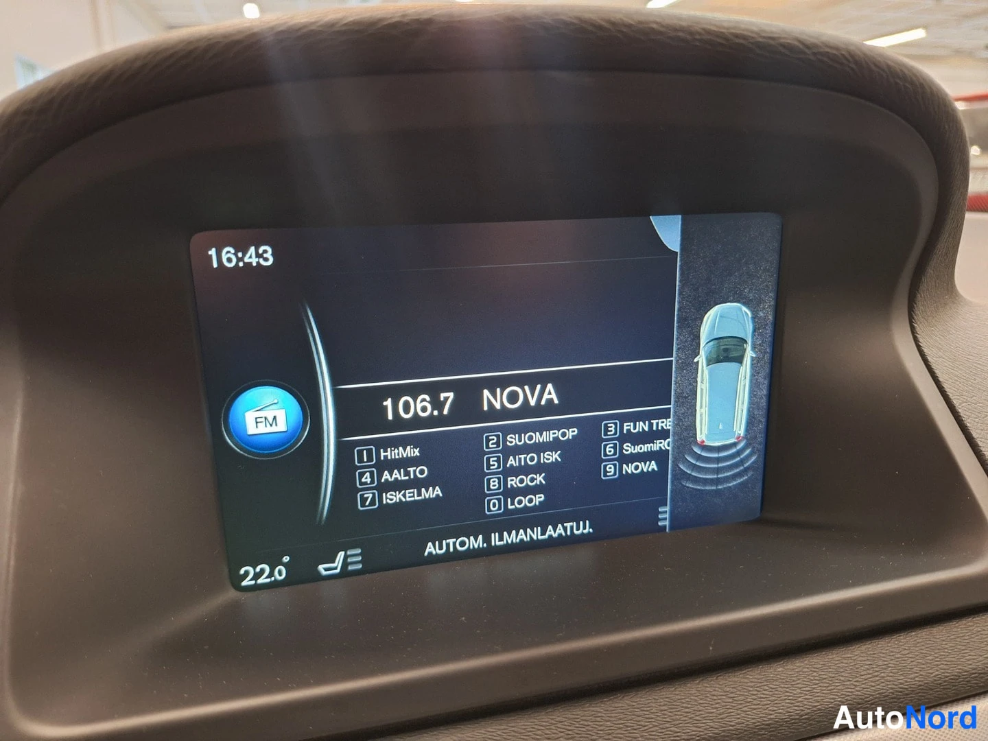 Yksityiskohta: Auton kojelaudan infotainment-näyttö, jolla radio CANAL 106,7 NOVA ja ajoneuvon takaosan tutkakuva.