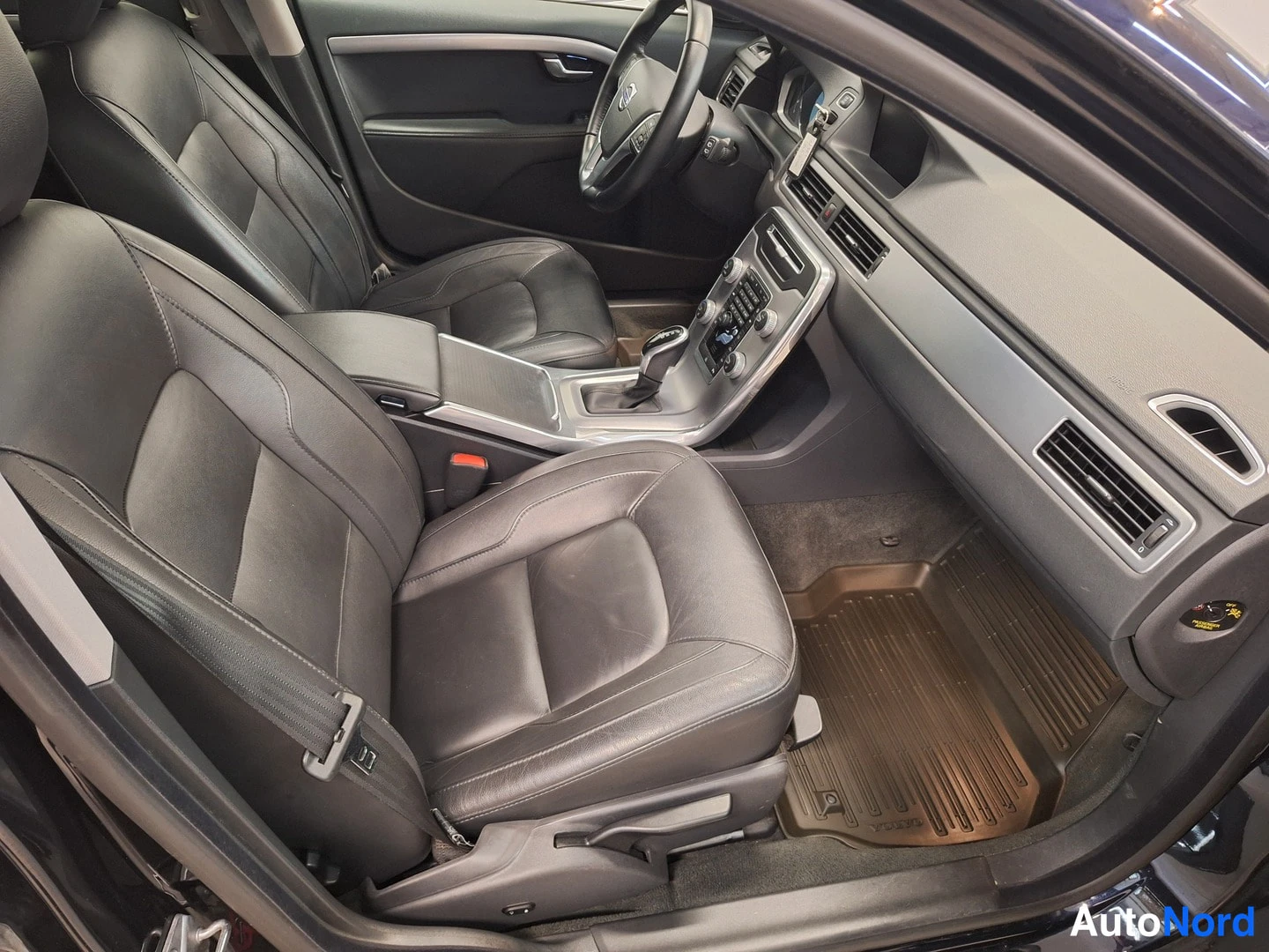 Muu: Volvo V70:n sisätilat etumatkalta: mustat nahkaistuimet, keskusconsole ja automaattivaihteisto, kellertävä askelmatto.