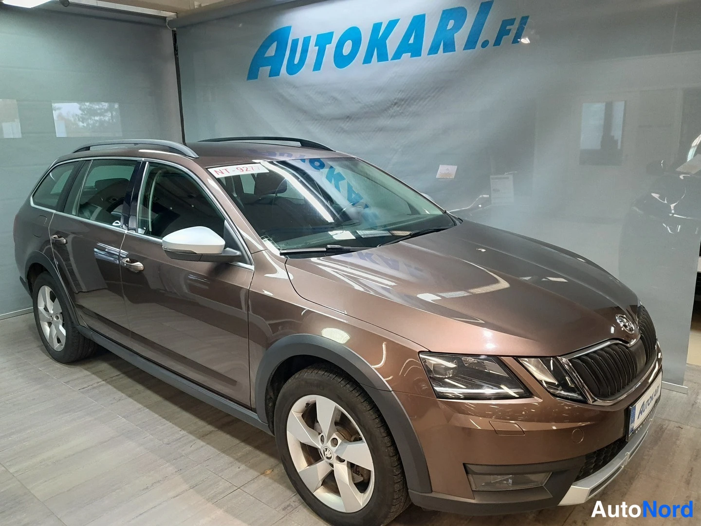 Etuviisto, nokka oikealle: Ruskea Skoda Octavia Combi farmari etukulmasta, keulagrafiikka ja kylki näkyvissä myymälätilassa.