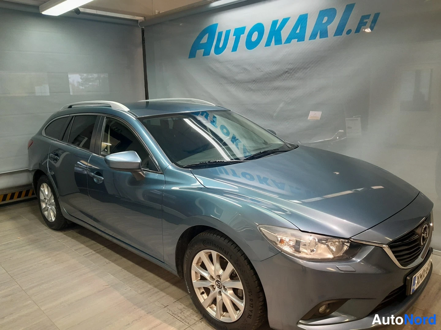 Etuviisto, nokka oikealle: Sinertävänharmaa Mazda 6 -farmariauto Autokari.fi-hallissa, etukulmasta oikealta