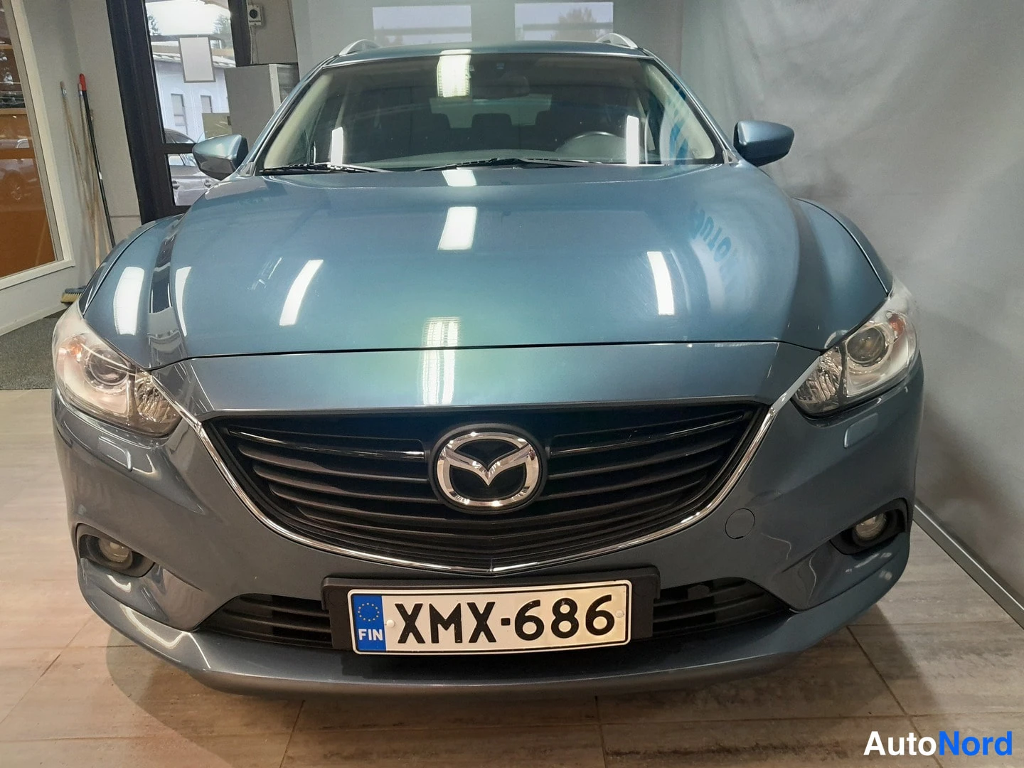 Edestä: Sinertävänharmaan Mazda 6 -farmarin etunäkymä sisätiloissa, rekisterikilpi.