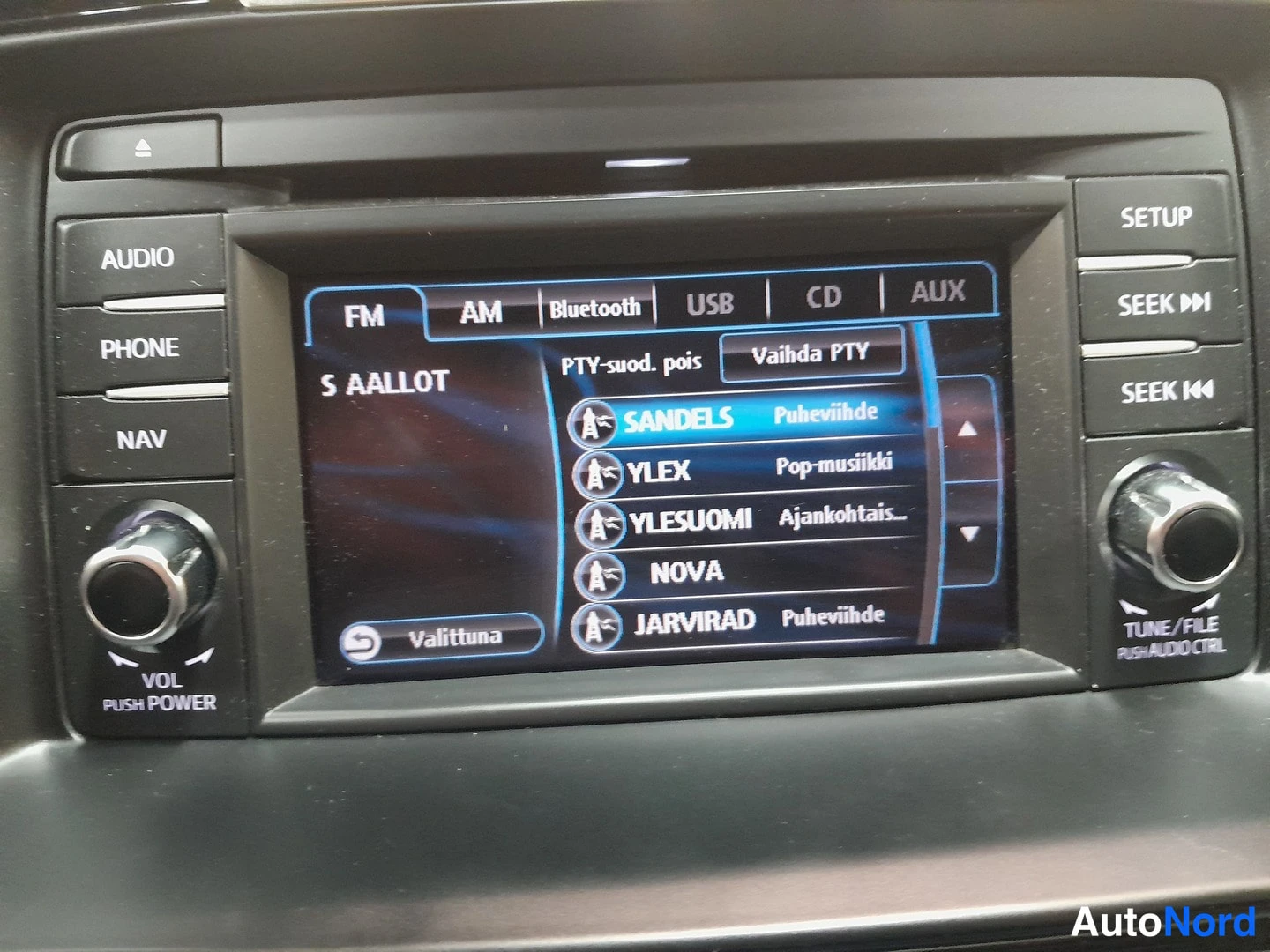 Muu: Auton radiopaneelin näyttö AM-aaltoasemaluettelolla, lähdetyyppeinä Bluetooth, USB, CD ja AUX