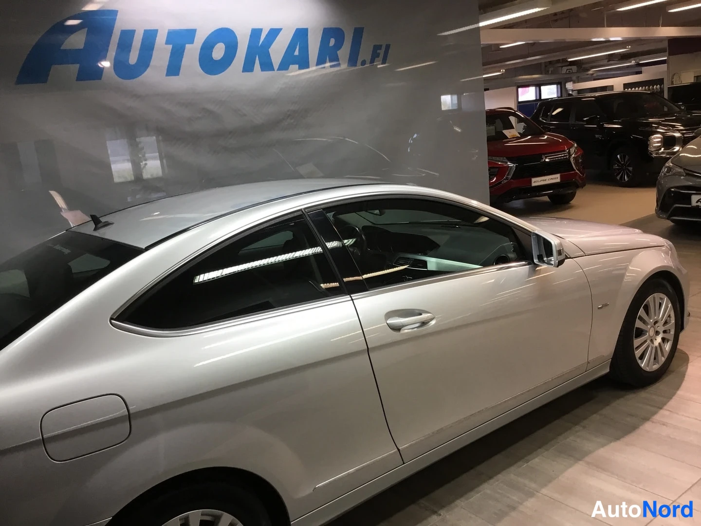 Sivulta: Sivukuva hopeisen Mercedes-Benz C-sarjan coupén vasemmasta sivusta autonäyttelytilassa.