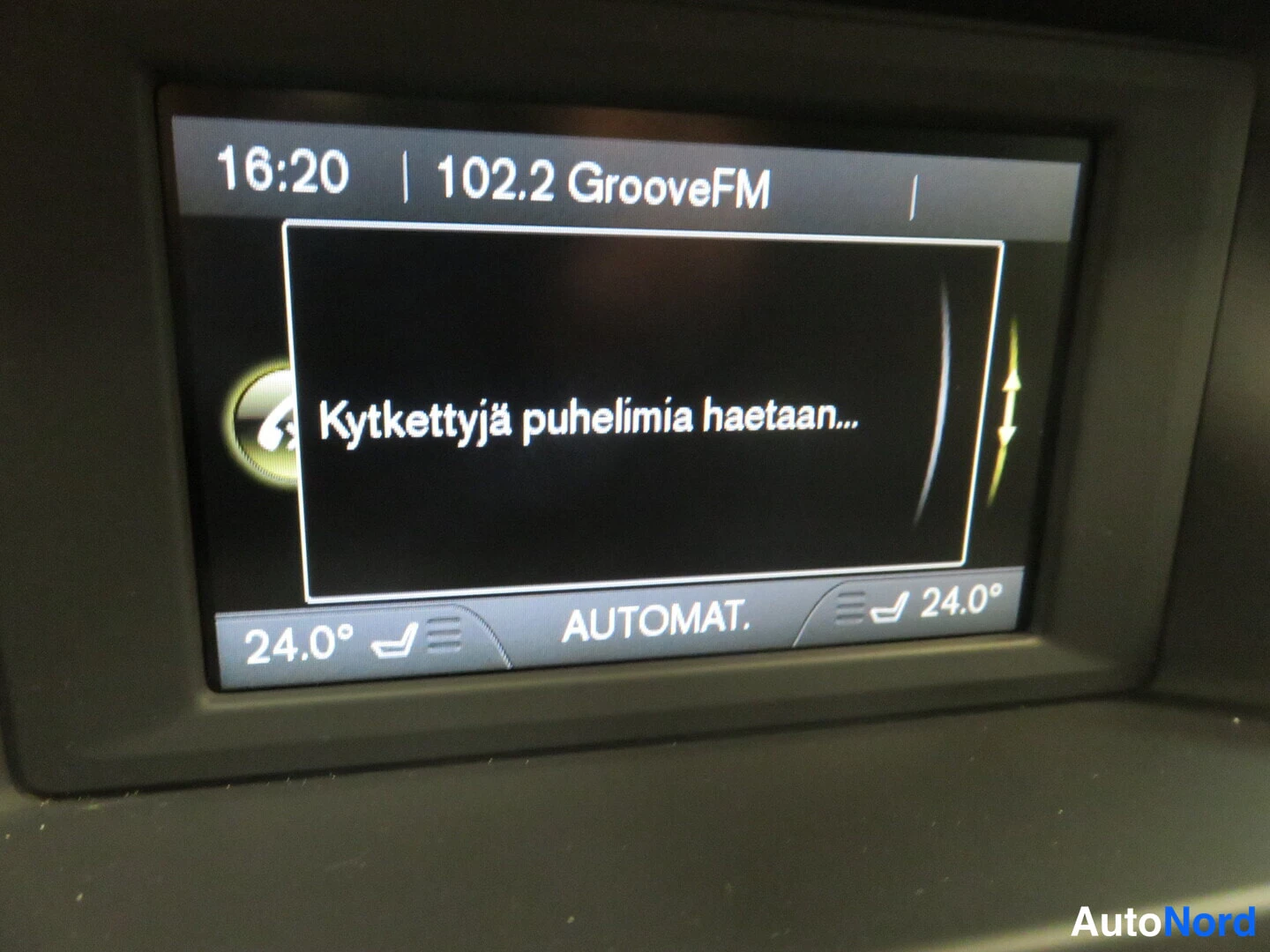 Muu: Auton kojelaudan näyttö näyttää radion 102.2 GrooveFM ja tekstin 'Kytkettyjä puhelimia haetaan…', lämpötila 24.0 astetta ja AUTOMAT.