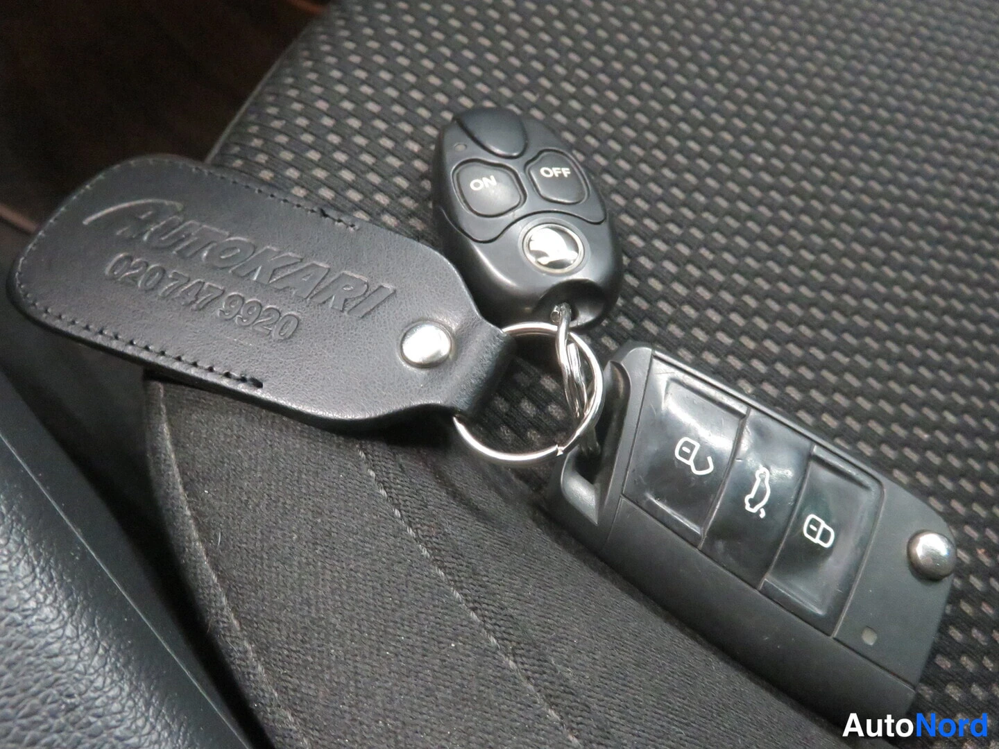 Yksityiskohta: Sisätilakuvassa kaksi avainnarua ja nahkainen avainnippu, jossa lukee AUTOKARI 0207479920, mustalla kuviollisella verhoilulla.
