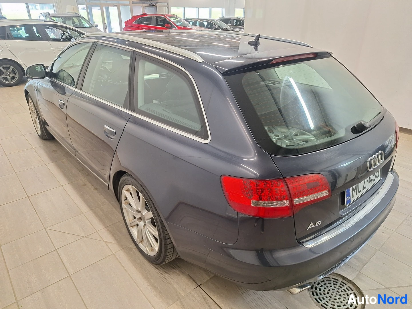 Takaviisto: Rear three-quarter view of a dark blue Audi A6 Avant featuring red taillights, an 'A6' badge, silver roof rails, and tinted rear windows. The license plate read
