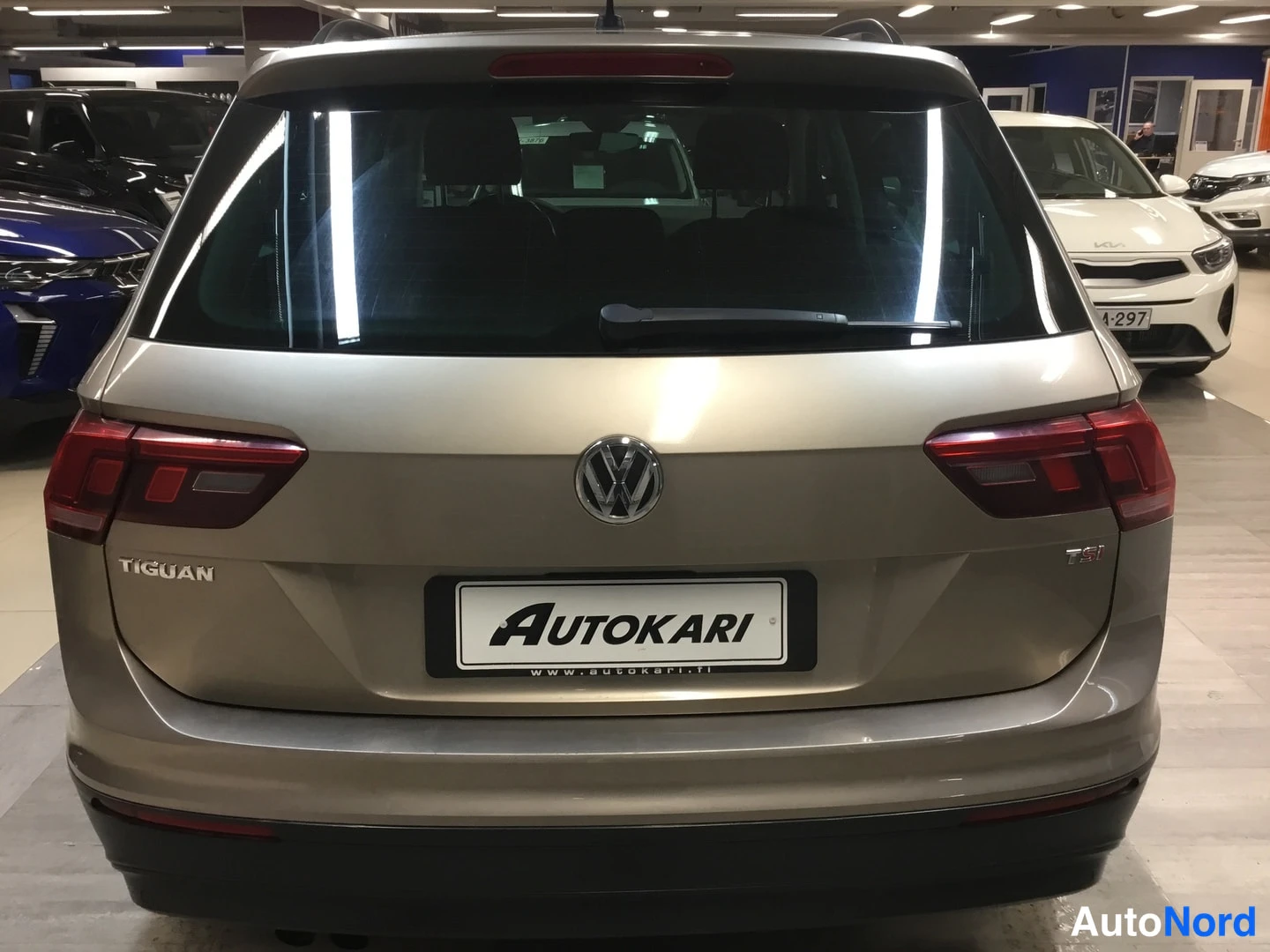 Takaa: Volkswagen Tiguinin takaosa suoraan takaa: takavalot, portaan VW-merkki ja TIGUAN-teksti näkyvät, auto on beige-kultainen.