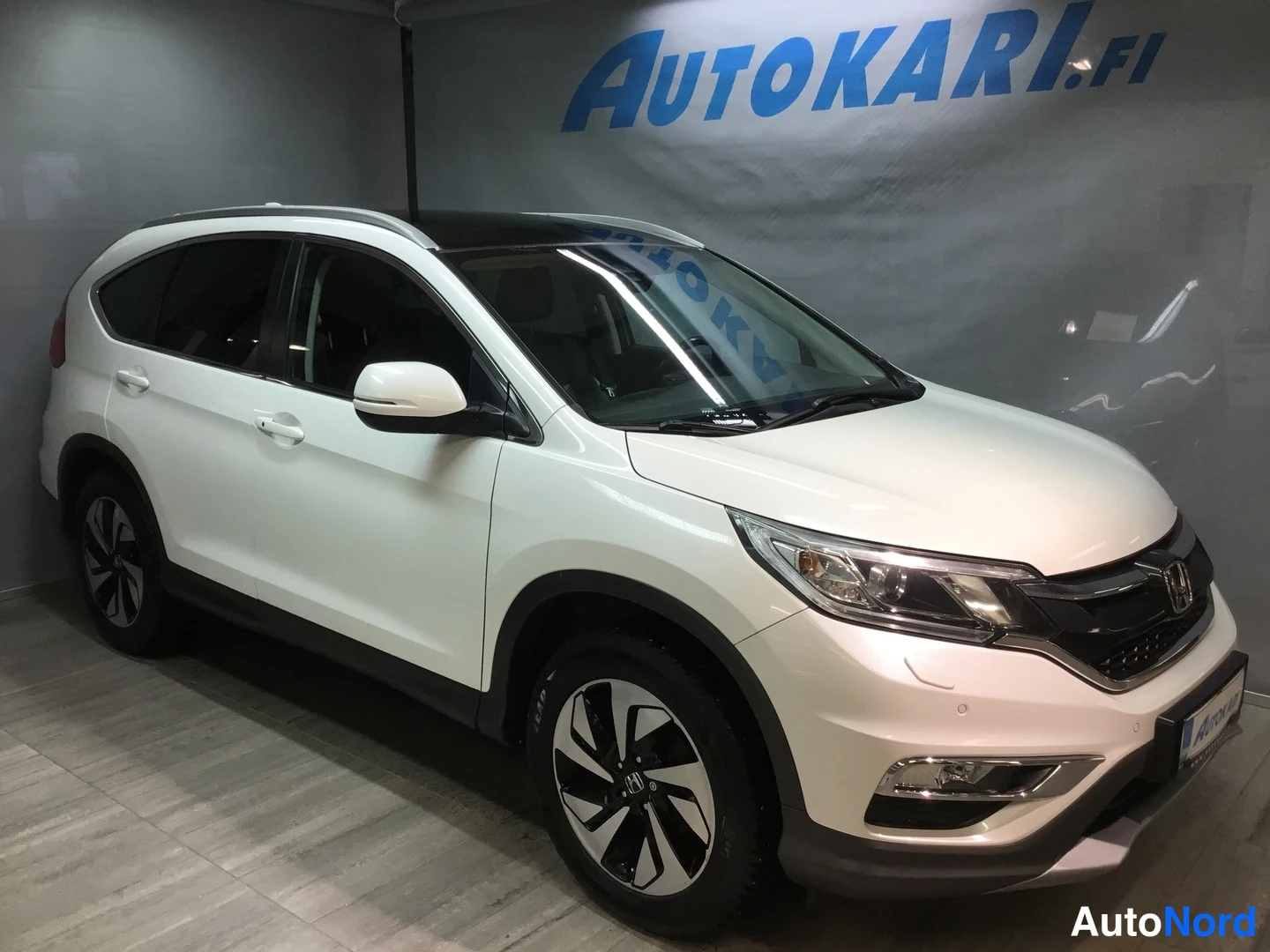 Etuviisto, nokka oikealle: Valkoinen Honda CR-V etuviistosta oikealta kuvattuna automaatiossa; kuvassa näkyvät etusäleikkö ja ajovalot, molemmat sivut ovista ja urheilullisista kev
