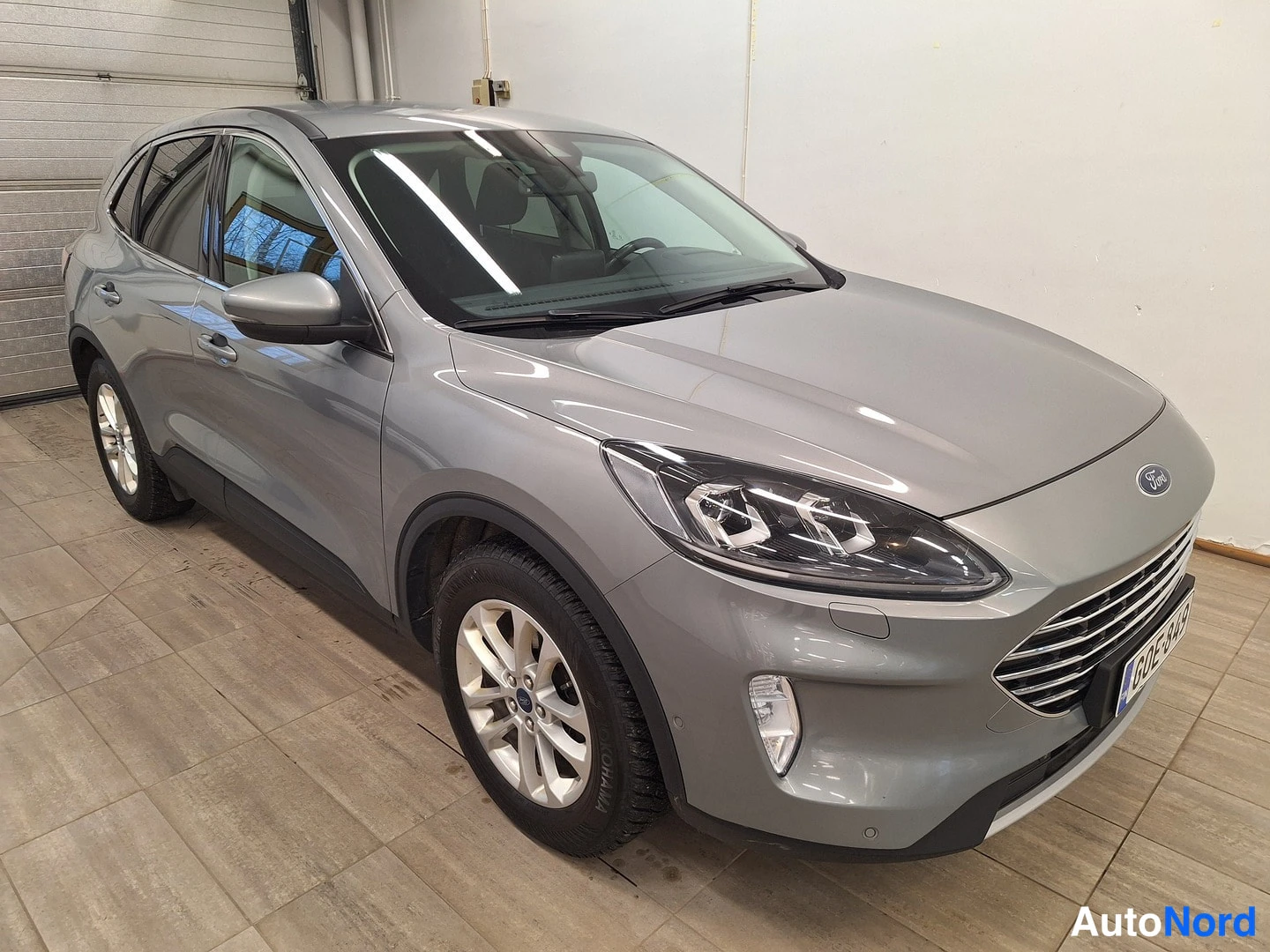 Etuviisto, nokka oikealle: Hopeanharmaa tila-auto etuviistosta oikealta, showroomissa