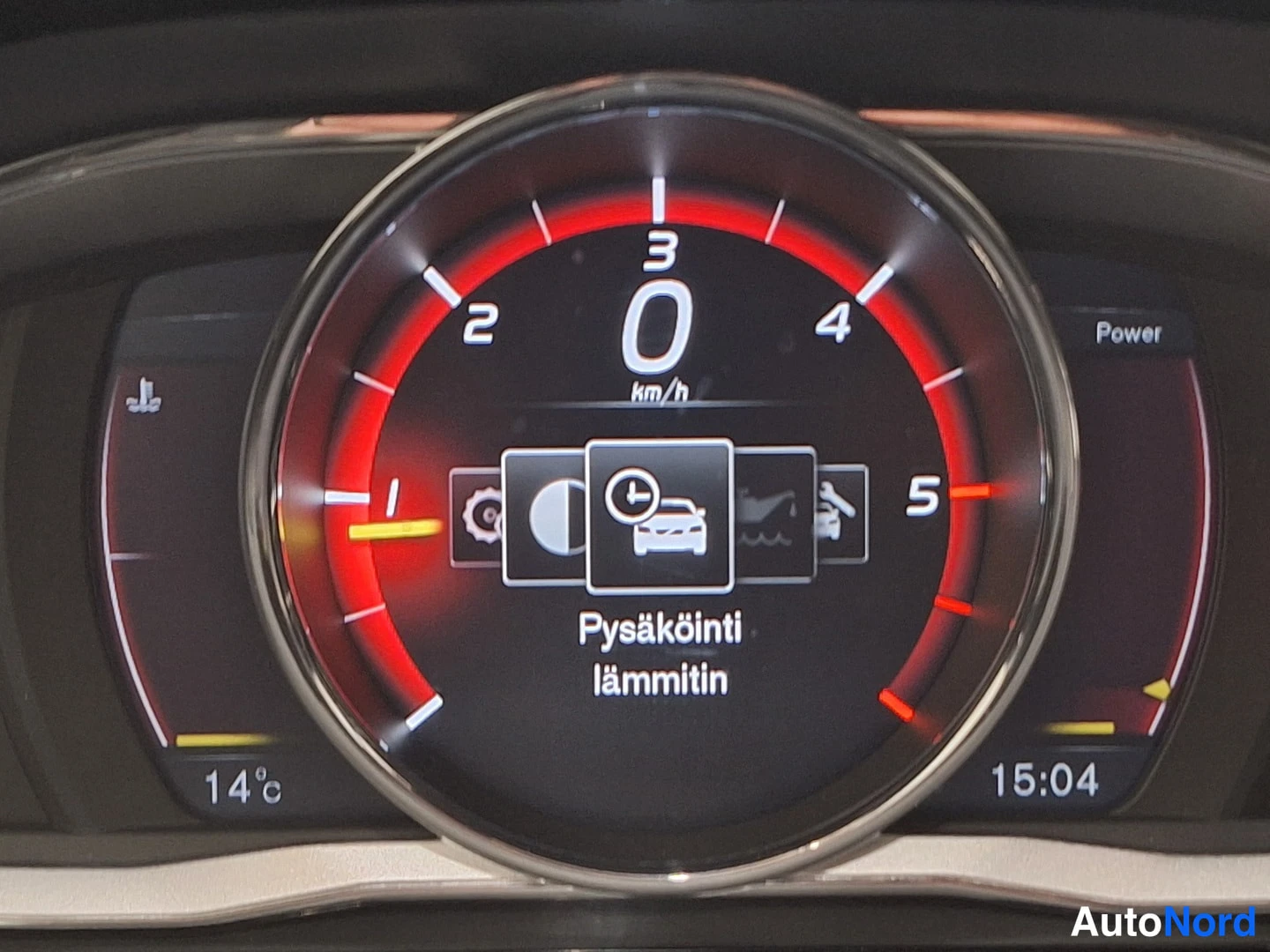 Muu: Kojelaudan mittariston suhde: nopeusmittari näyttää 0 km/h, näytöllä lukee 'Pysäköinti lämmitin', kellonaika 15:04 ja lämpötila 14°C.