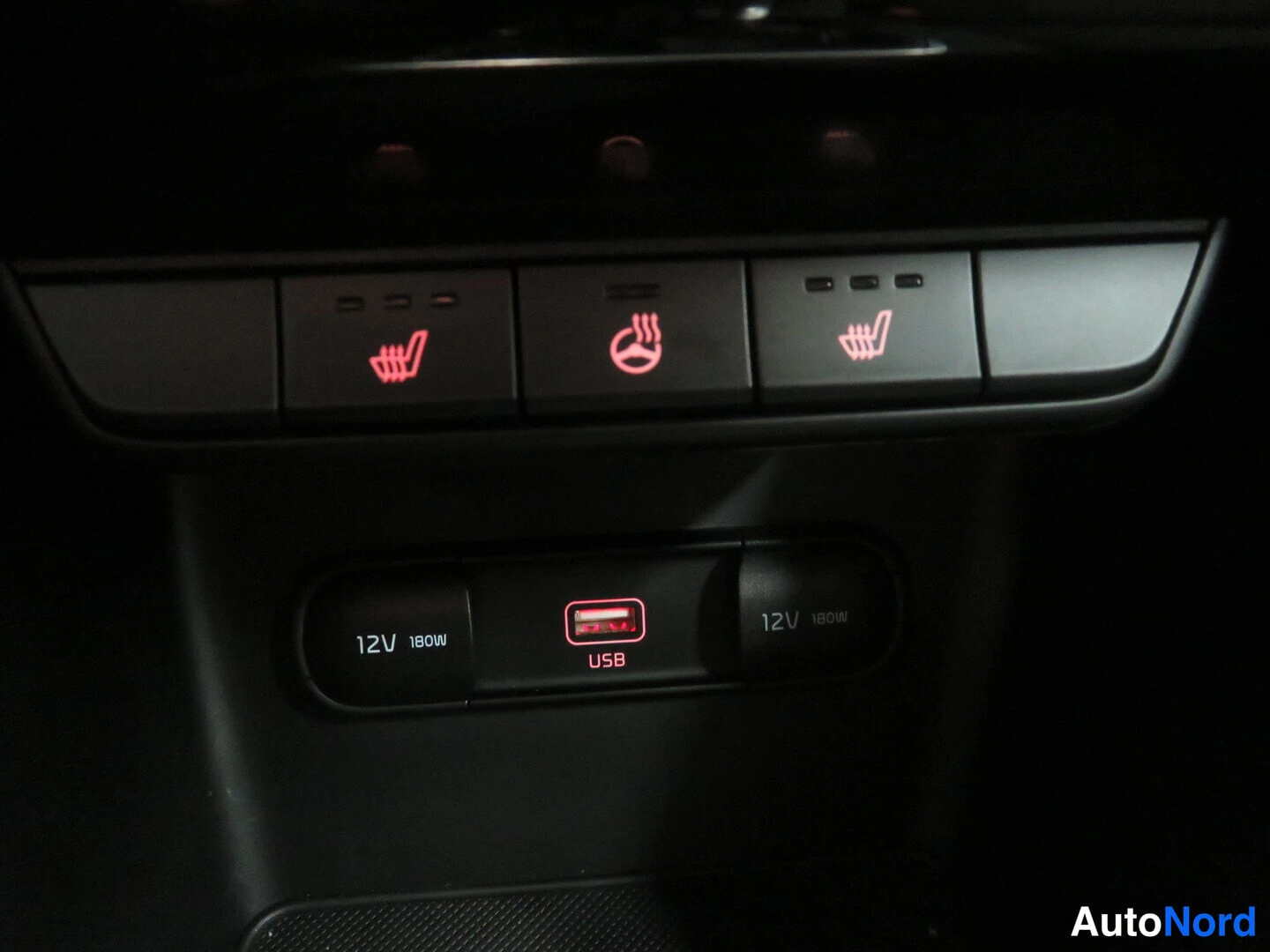 Yksityiskohta: Pimeässä kuvattu keskiöpaneeli: kaksi punaisin merkkivaloin palavaa istuinlämmityspainiketta ja valaistu USB-portti sekä kaksi 12V 180W pistorasiaa.
