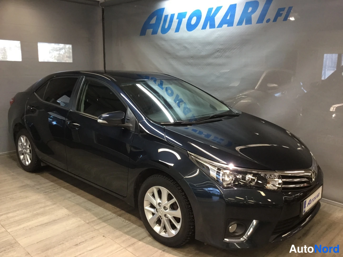 Etuviisto, nokka oikealle: Tummansininen sedan auto sivulta-etuviistöstä oikeaan suuntaan katsottuna auton sisätiloissa.