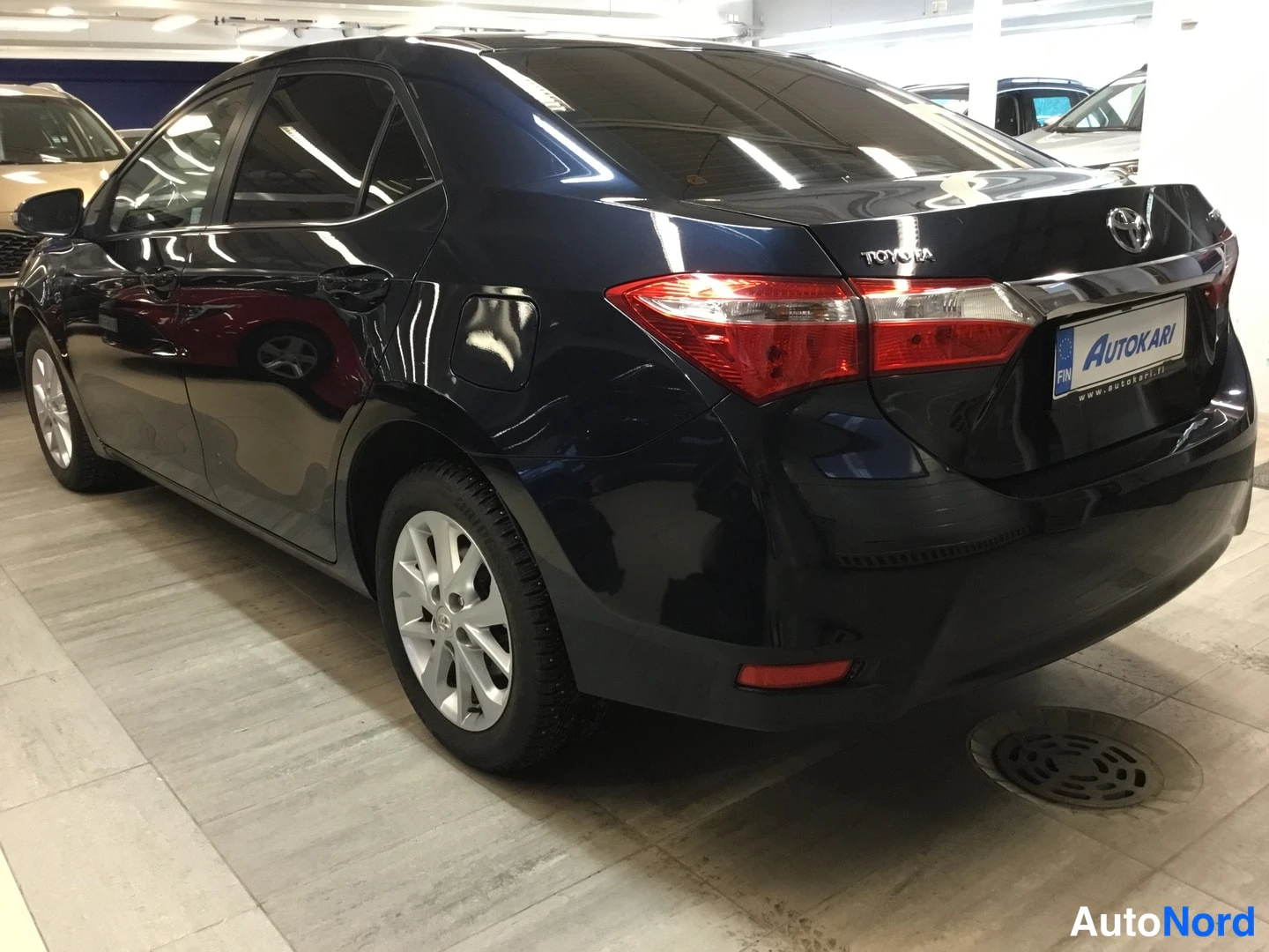 Takaviisto: Tummansininen sedan auto takaviistöstä katsottuna auton myyntitilassa, Toyota-merkintä takakannella.