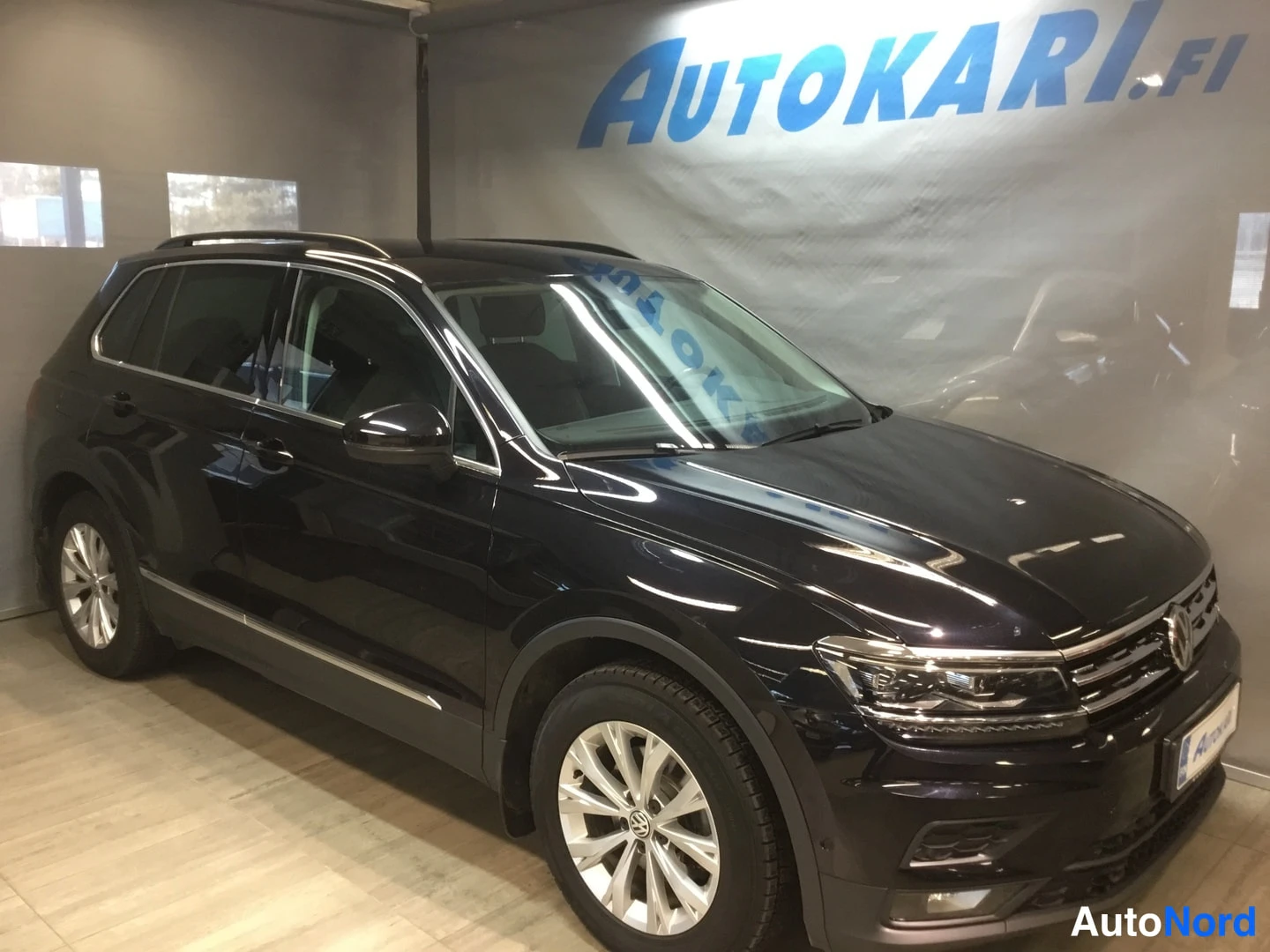 Etuviisto, nokka oikealle: Mustan Volkswagen Tiguanin etukolmattakuva sisätiloissa, etusäleikkö ja oikea kylki näkyvissä.