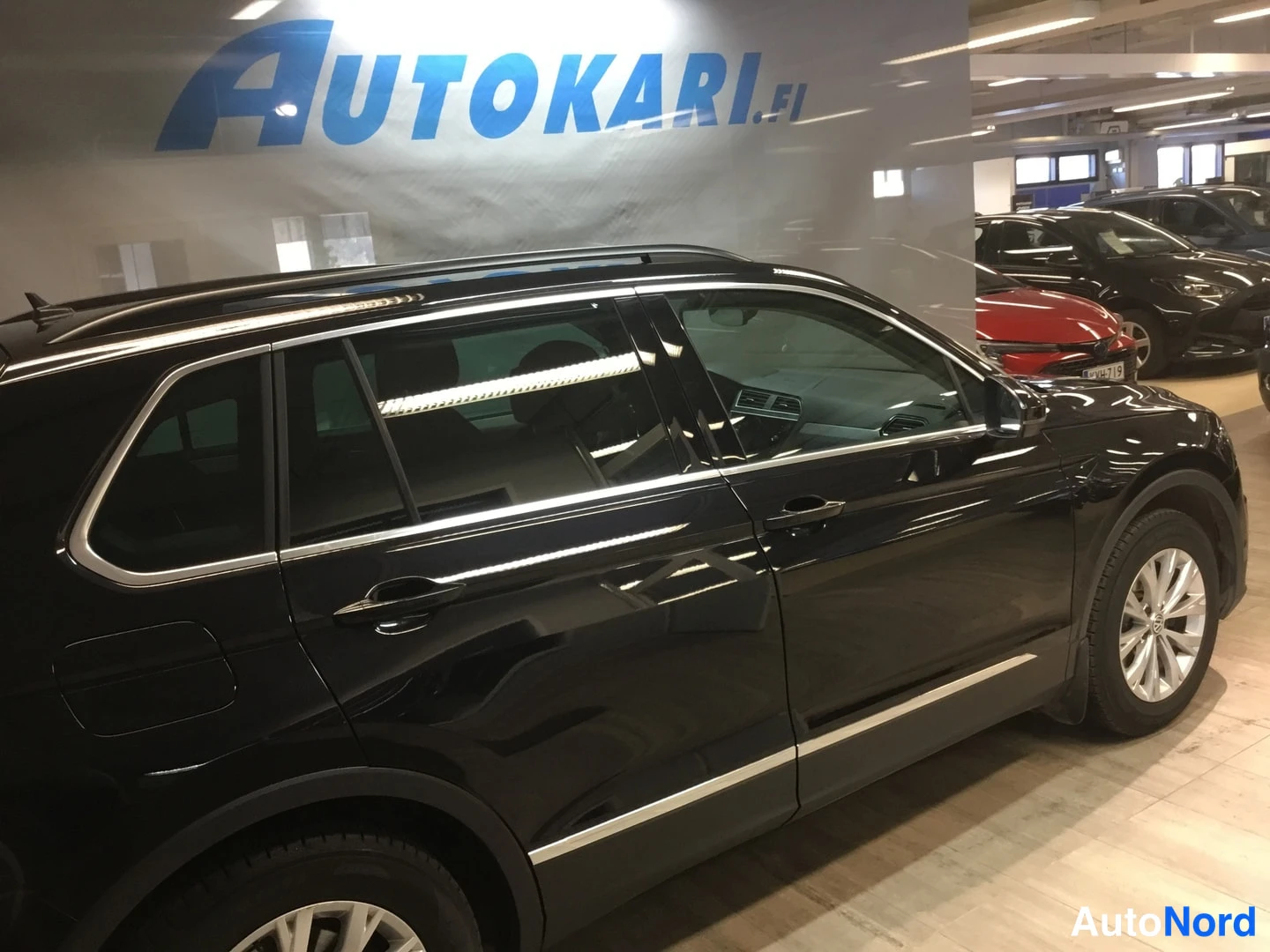 Sivulta: Mustan Volkswagen Tiguanin sivukuva autosalissa, oikea kylki ja pyörät näkyvissä.