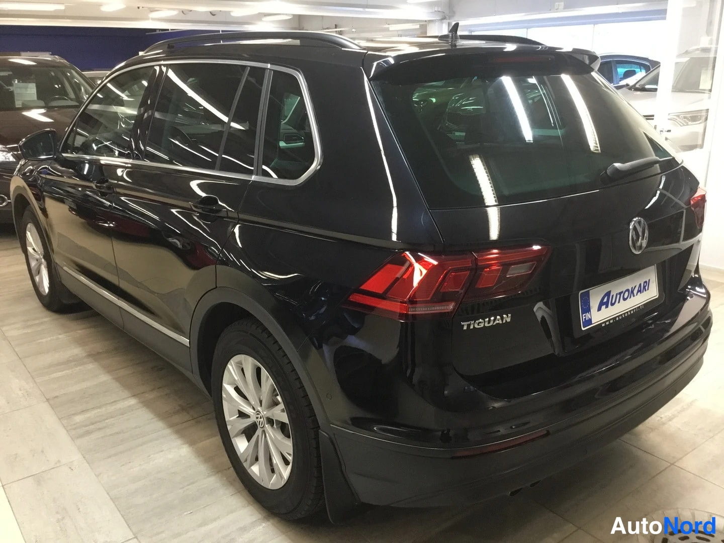 Takaviisto: Mustan Volkswagen Tiguanin takakolmattakuva sisätiloissa, takavalot ja Tiguan-tunnus näkyvissä.