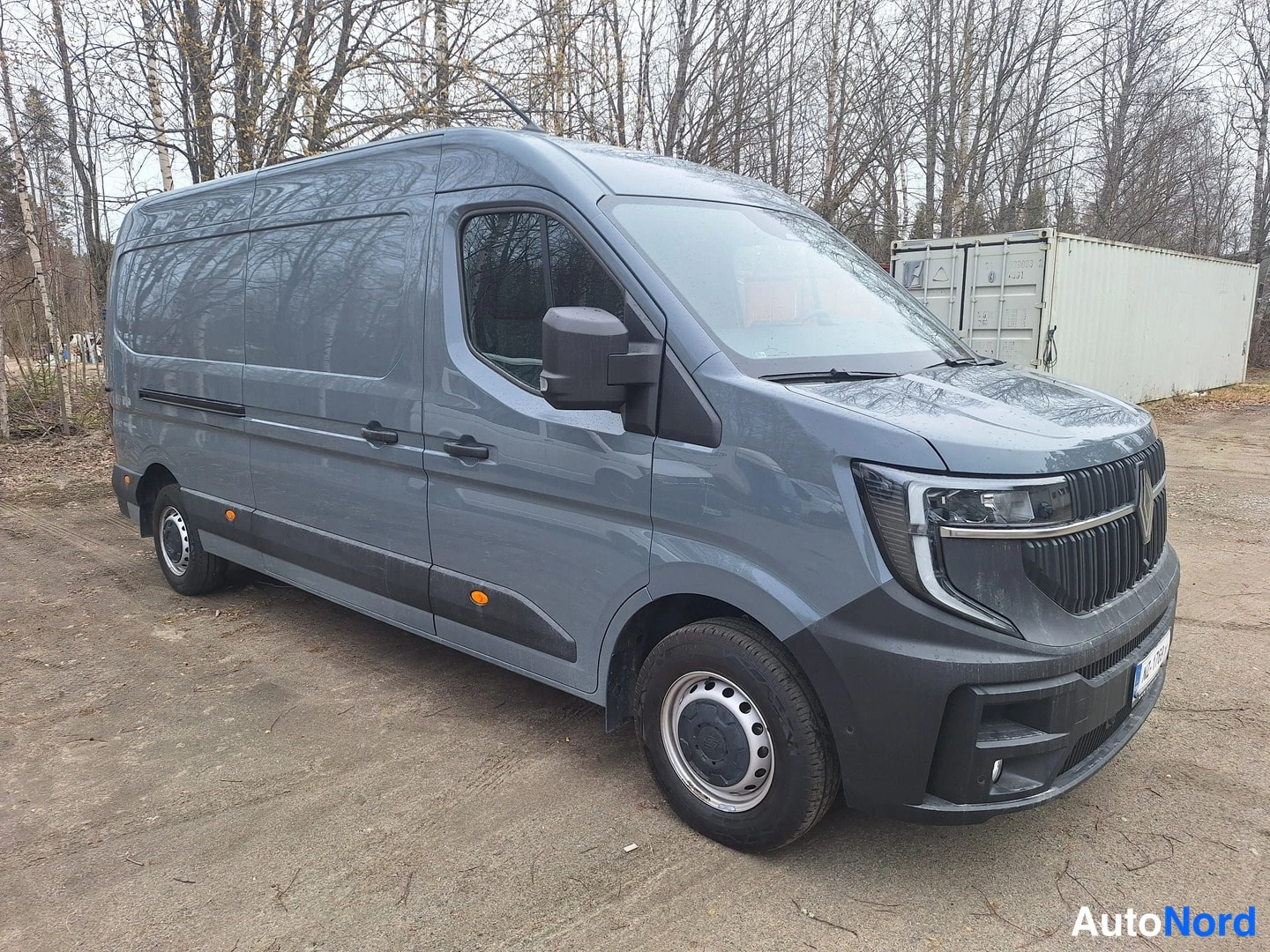 Etuviisto, nokka oikealle: Harmaa Renault Master -pakettiauto etukulmasta oikealta kuvattuna metsäisellä sorapihalla.