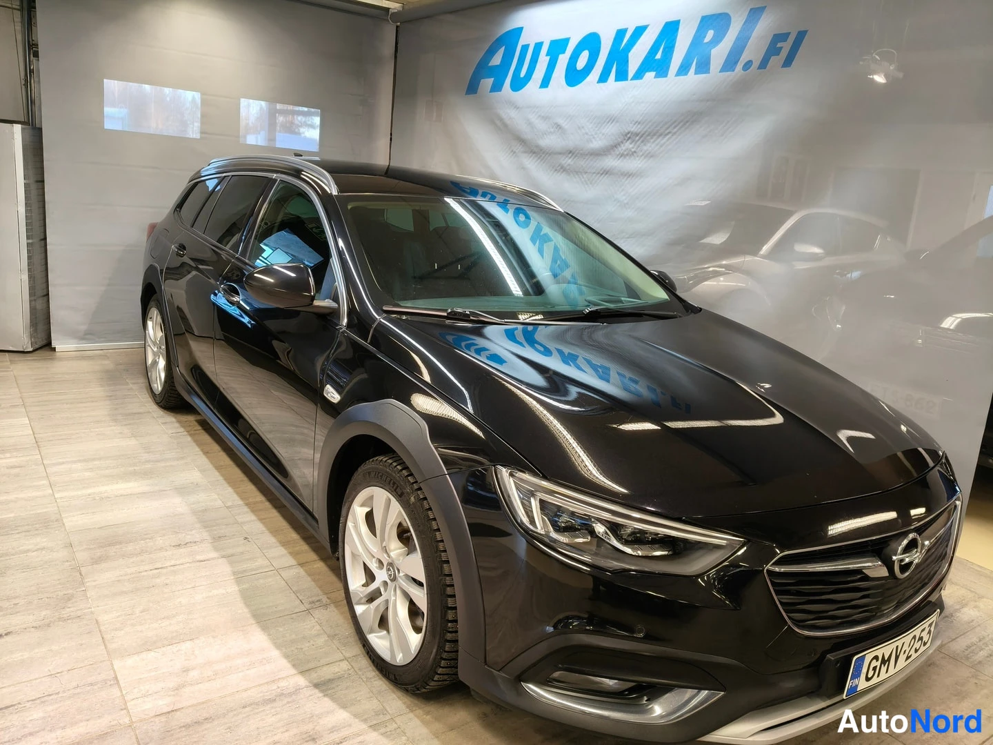 Etuviisto, nokka oikealle: Mustan farmariauton etukulma kuvattuna sisätiloissa, etusäleikkö ja oikea kylki näkyvät, rekisterikilpi.