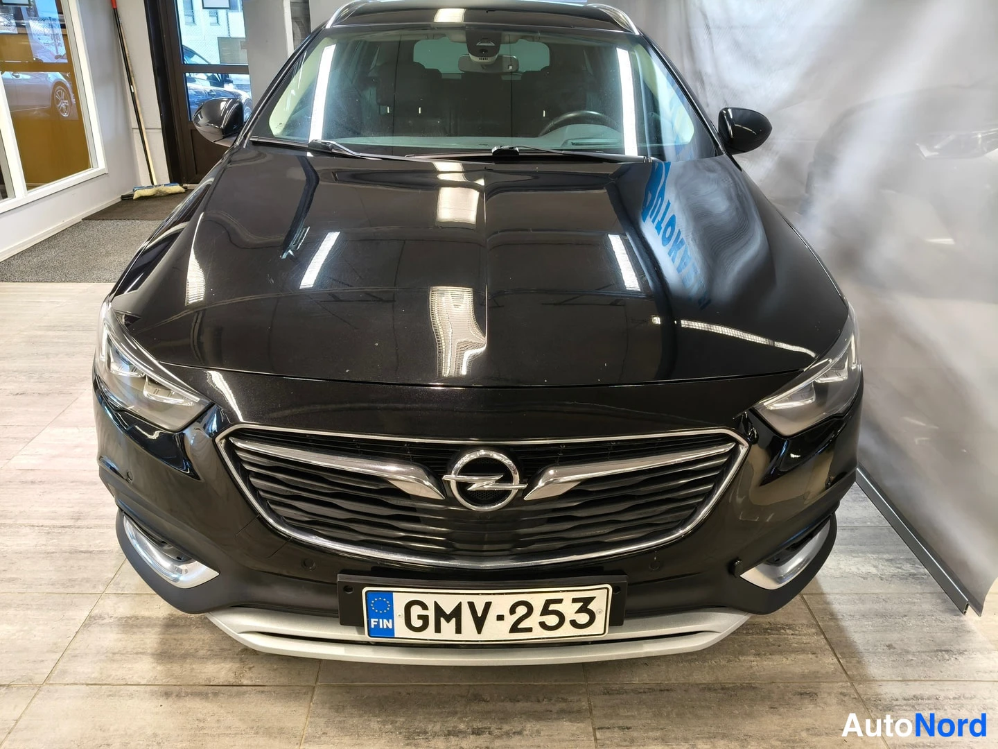 Edestä: Mustan farmariauton etunäkymä suoraan edestä, Opel-merkki säleikössä ja rekisterikilpi.