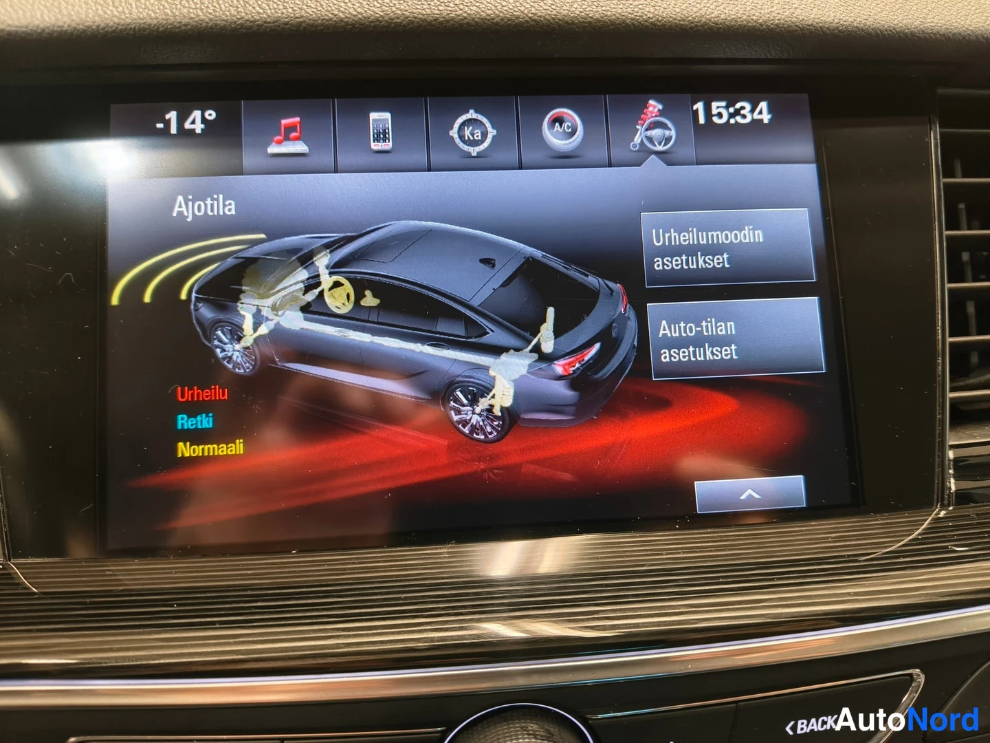 Yksityiskohta: Auton kojelaudan infotainment-näyttö näyttää Ajotila-valikon, jossa on kuvitus auto ja valinnat Urheilu, Retki ja Normaali; oikealla Urheilumoodin asetukset ja