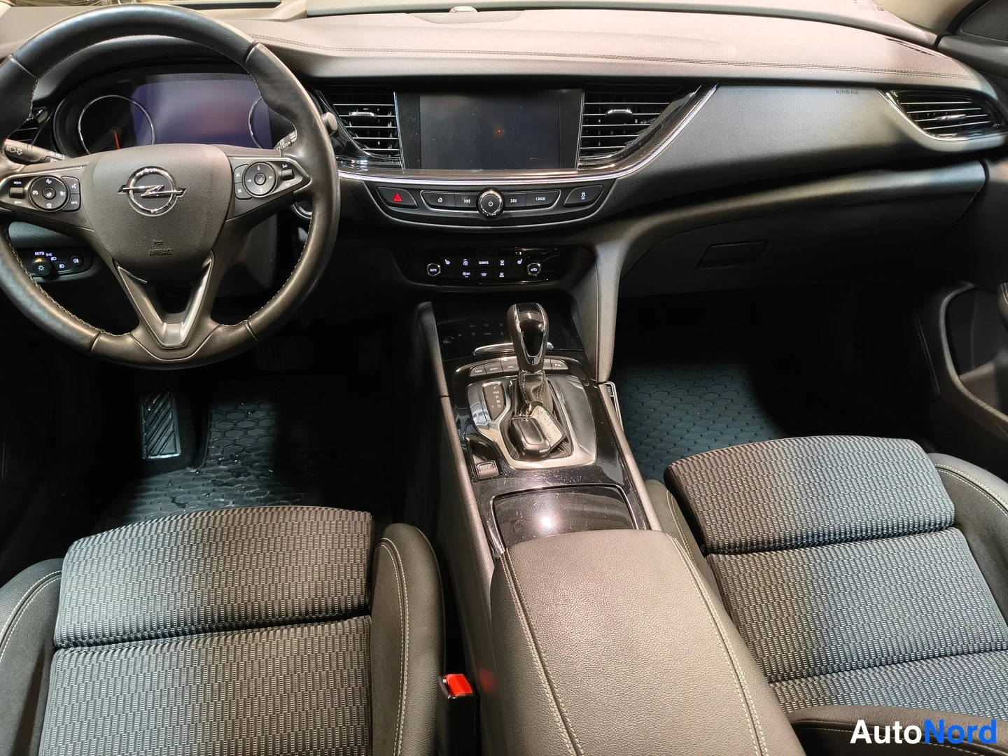 Etuviisto: Ohjaamo vasemmalta: Opel-merkkinen ohjauspyörä, keskikonsoli automaattivaihteen valitsimella, infotainment-näyttö ja kaksi etuistuinta.