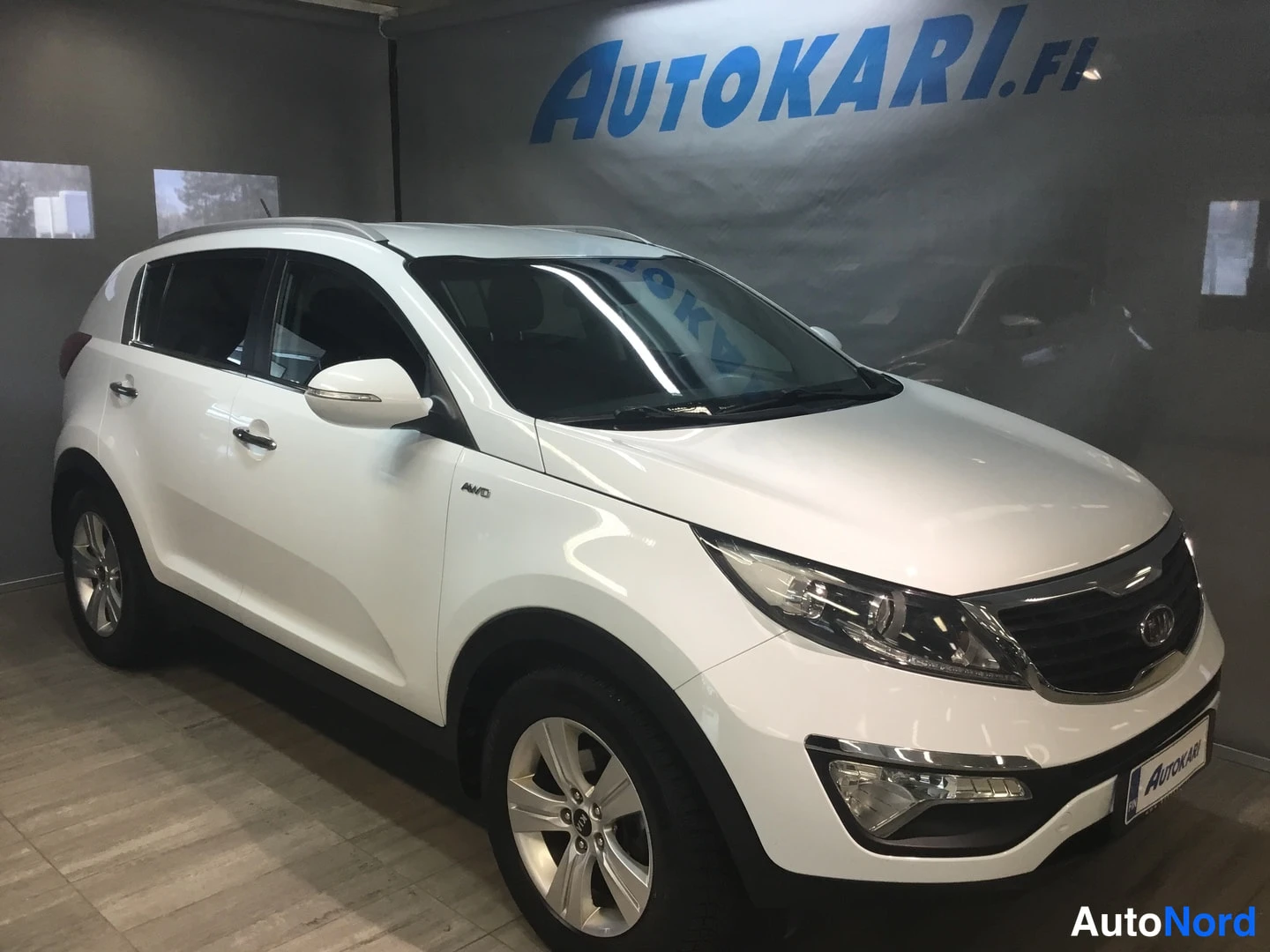 Etuviisto, nokka oikealle: Valkoinen KIA Sportage -maast-auto kuvattu etukulmasta autonose oikealla näkyen etupuskuri, ajovalot ja kylki.