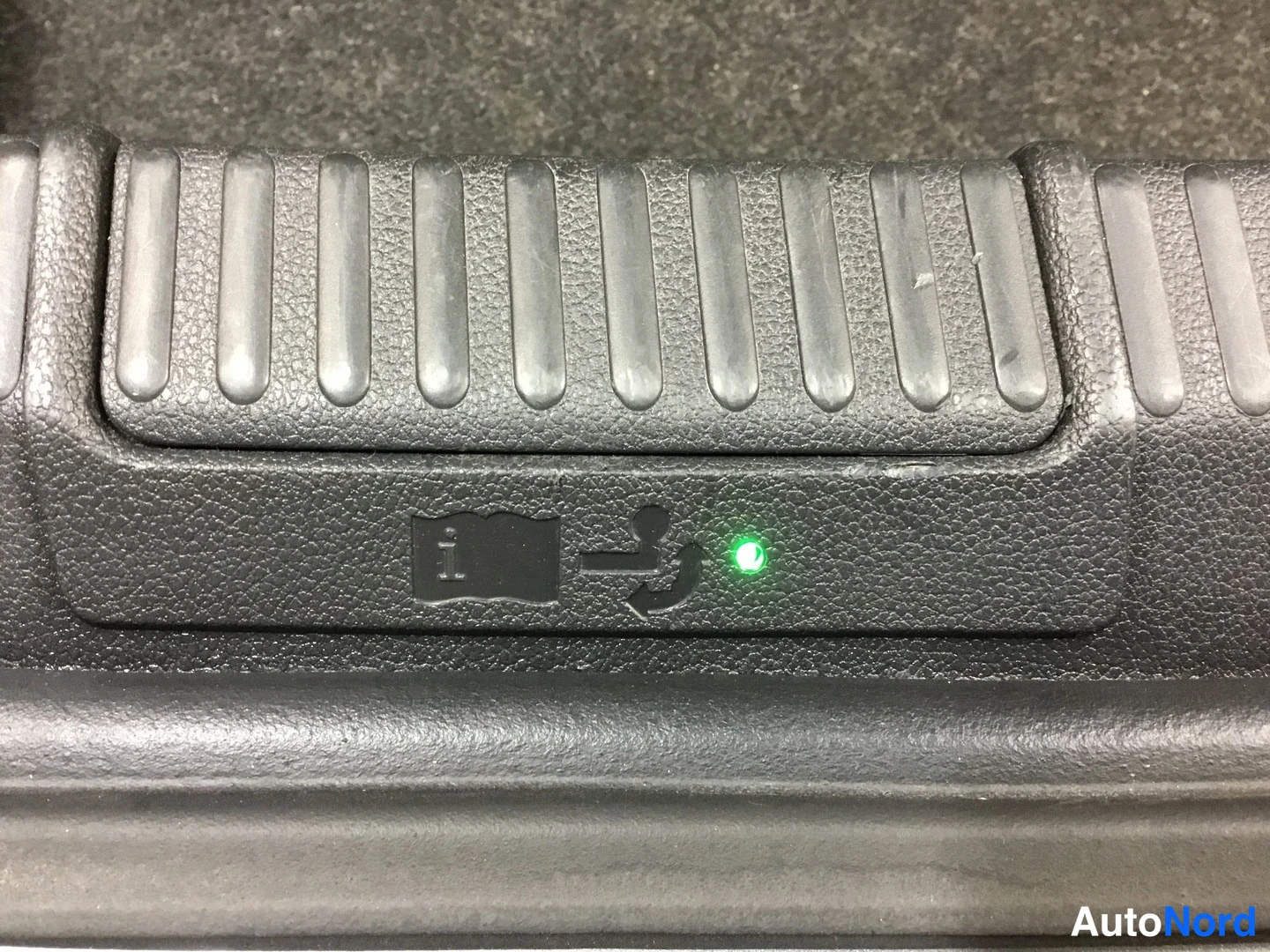 Yksityiskohta: Close-up of a black plastic ISOFIX child seat anchor point on the rear shelf with a green LED indicator light beside the symbol.