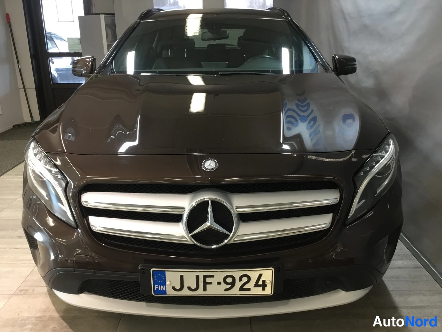 Edestä: Etuvuoto ruskeasta Mercedes-Benz GLA-autosta, jossa on suuri merkki eturistikkorivillä ja numero J-JF-924. Etusäleikön kaksi vaakasuoraa listaa ja valkoista ala