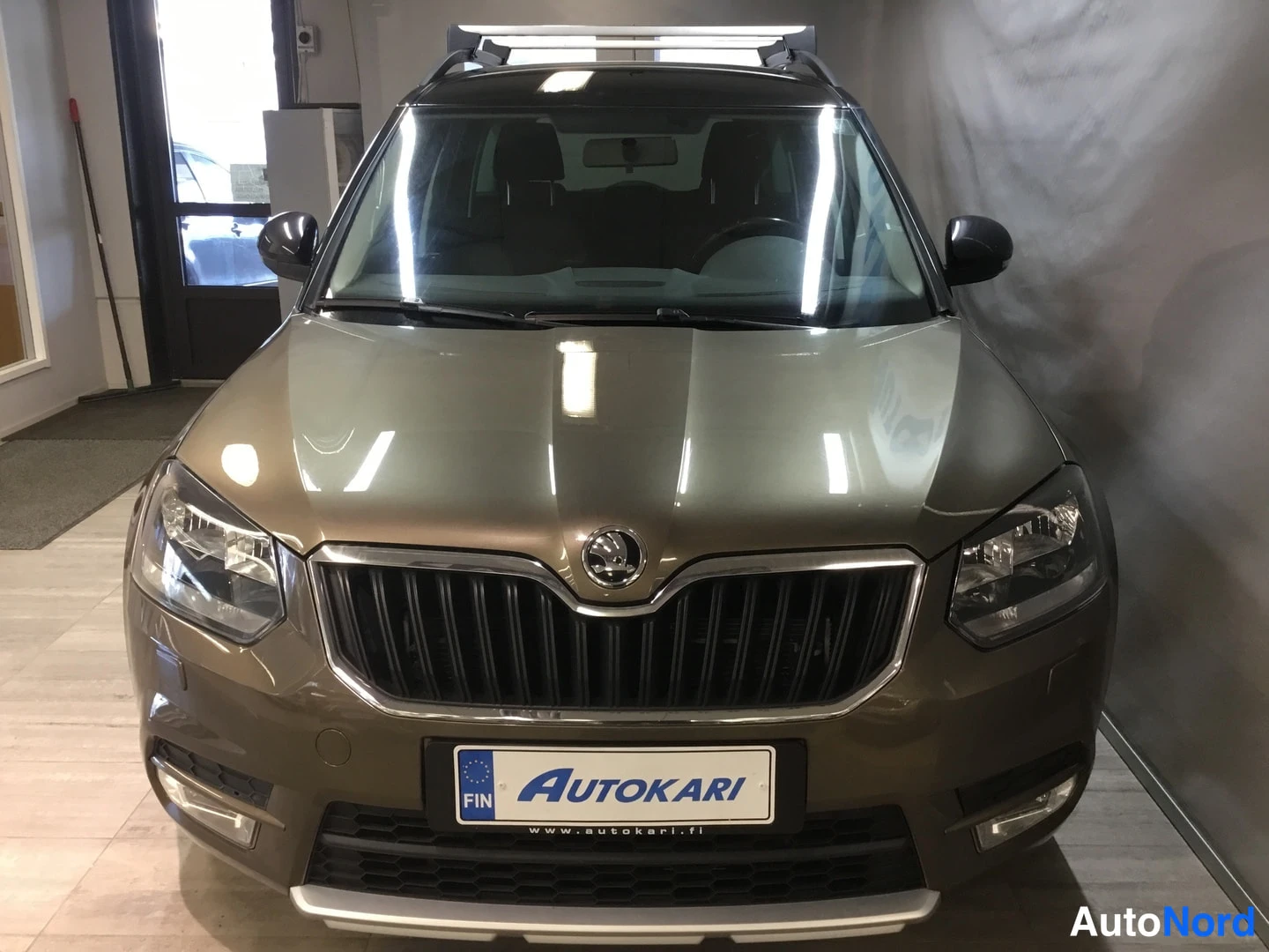 Edestä: Ruskean metallinhohtoinen Skoda Yeti suoraan edestä kuvattuna autohallissa.
