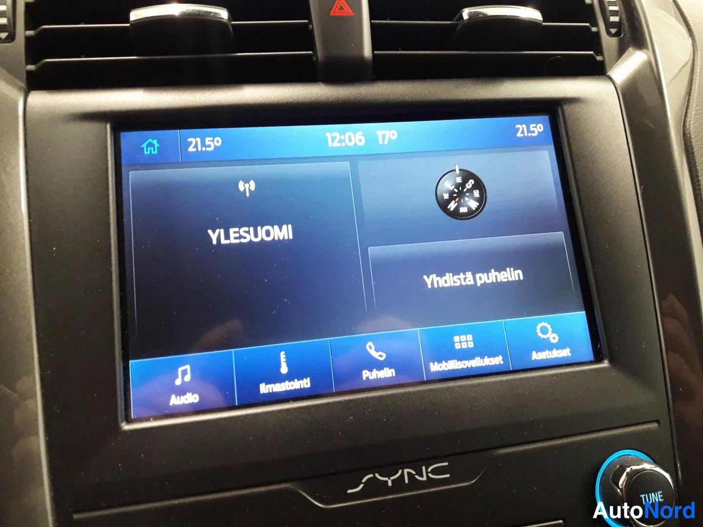 Yksityiskohta: Close-up of a central infotainment screen showing radio 'YLESUOMI' and phone connection prompt. Climate control temperature set to 21.5 degrees.