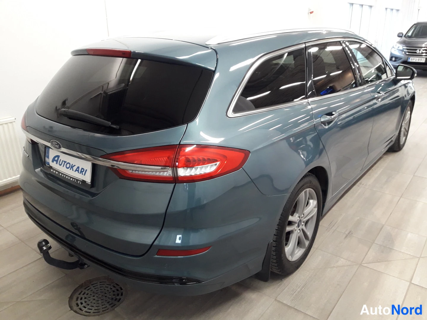 Sivulta: Side profile shot of Ford Mondeo showing rear quarter panel and taillight assembly. Blue-grey metallic paint with dark tinted windows and chrome window trim.