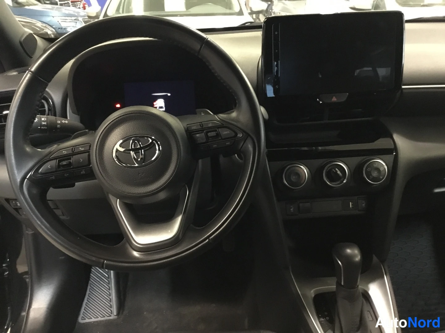 Muu: Toyota Yaris Crossin ohjaamo: Toyota-logollinen ohjauspyörä, keskellä kosketusnäyttö ja kolme säädönappia, automaattivaihteiston valitsin.