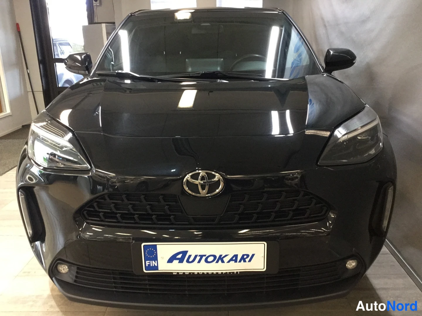Edestä: Mustan Toyota Yaris Crossin etupää suoraan edestä kuvattuna, Toyota-merkki kojelautanäytön ja Autokari-kyltin yllä.