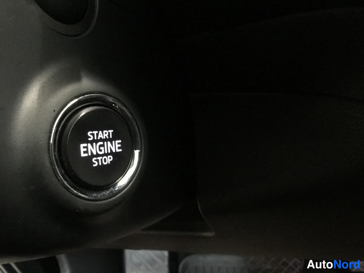 Yksityiskohta: Interior close-up of a push-button start/stop switch labeled 'START ENGINE STOP' in white text on a black surface, surrounded by a chrome trim ring.