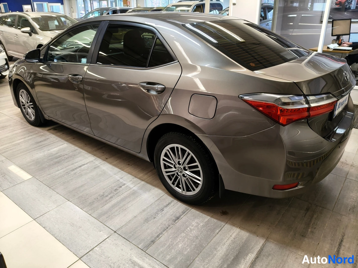 Takaviisto: Harmaa sedan autosalon lattialla takakulmasta nähtynä.