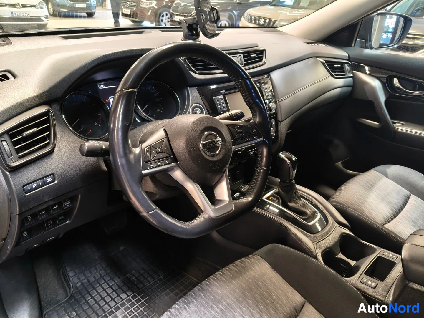 Sivulta: Nissan X-Trailin ohjaamo kuljettajan puolelta: Nissan-merkkinen ohjauspyörä, mittaristo, keskikonsolin näyttö ja automaattivaihteen valitsin.