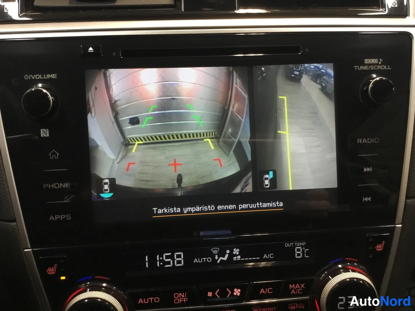Yksityiskohta: Infotainment screen displaying dual rear-view camera feeds (wide-angle left and narrow view right) with red, yellow, green guidelines. Finnish message 'Tarkista